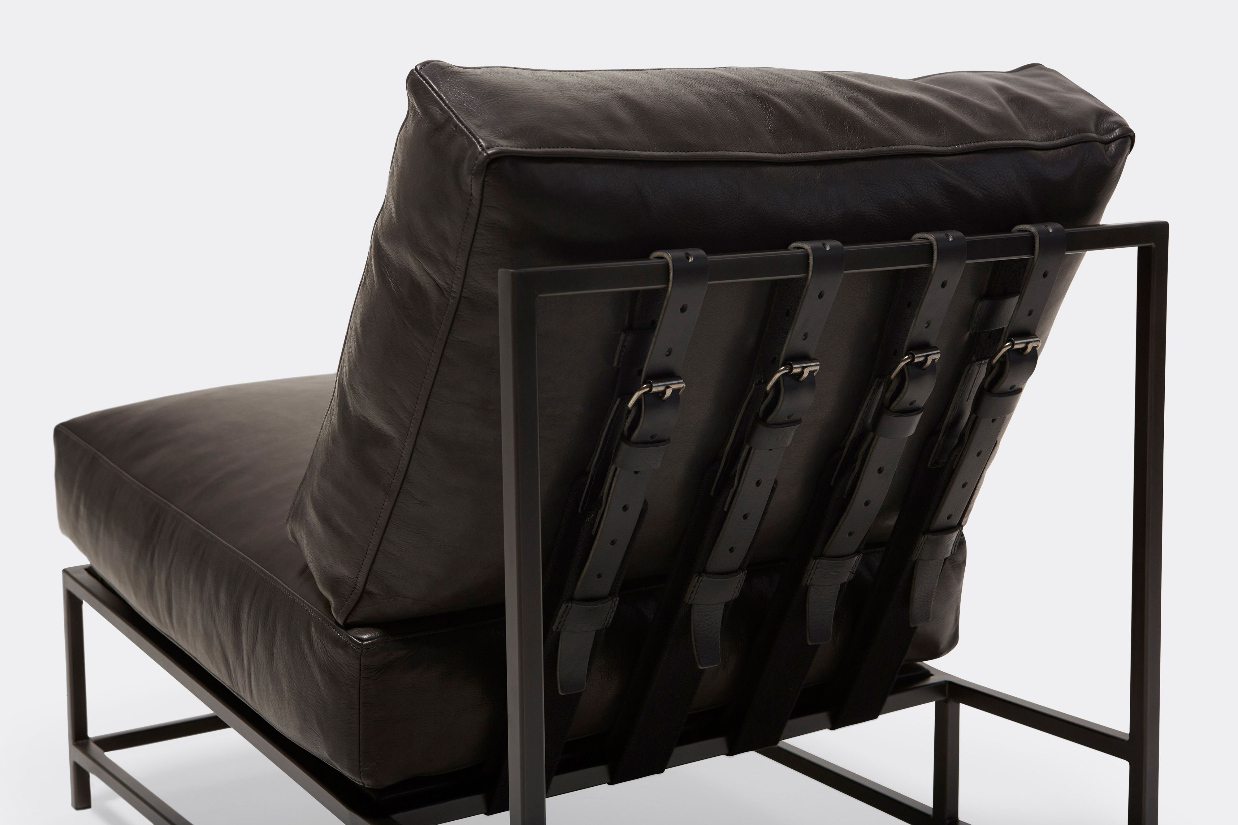 Back of lounge chair with black leather upholstery and black leather belts on black metal frame