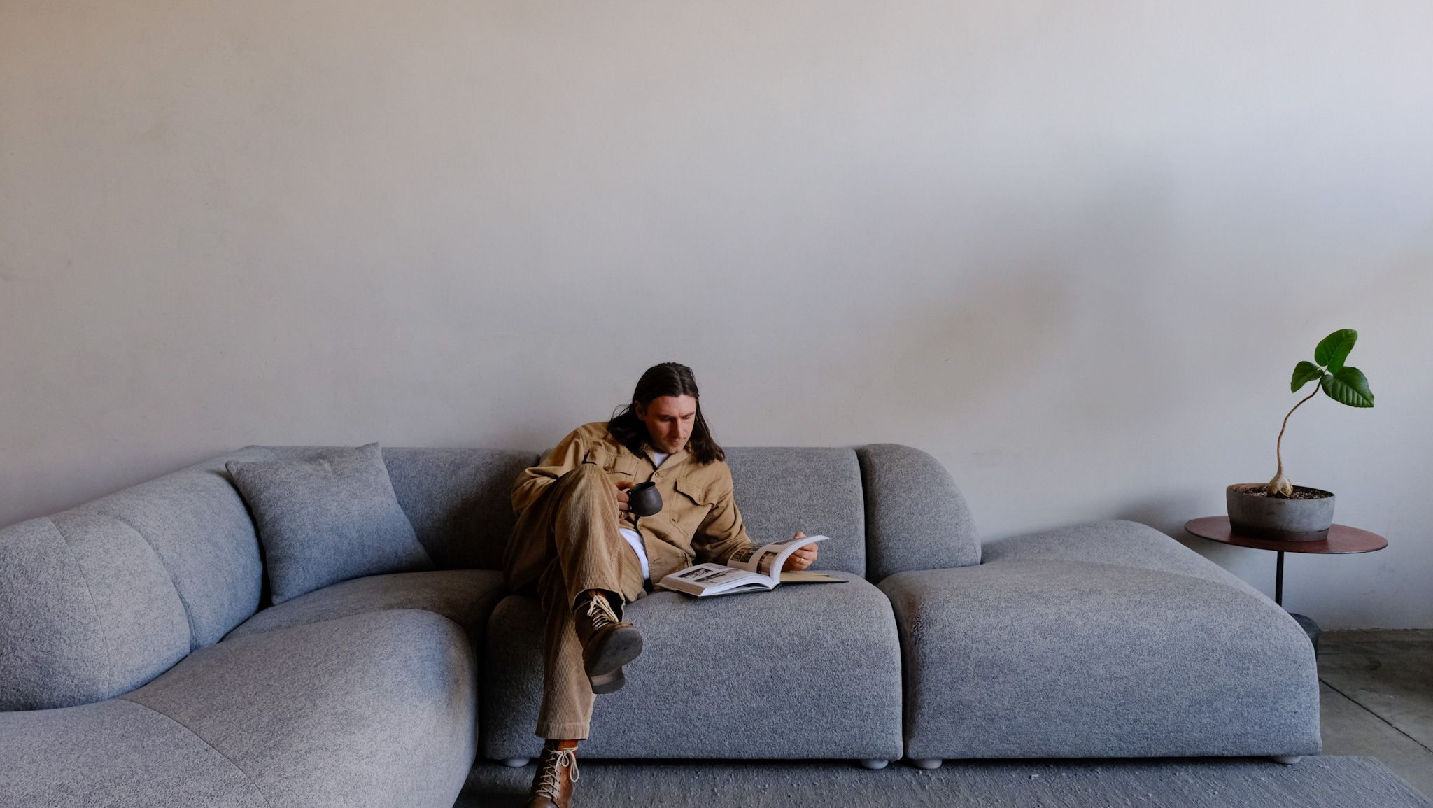 A person with long hair reads a magazine while sitting on a modern grey modular sofa.