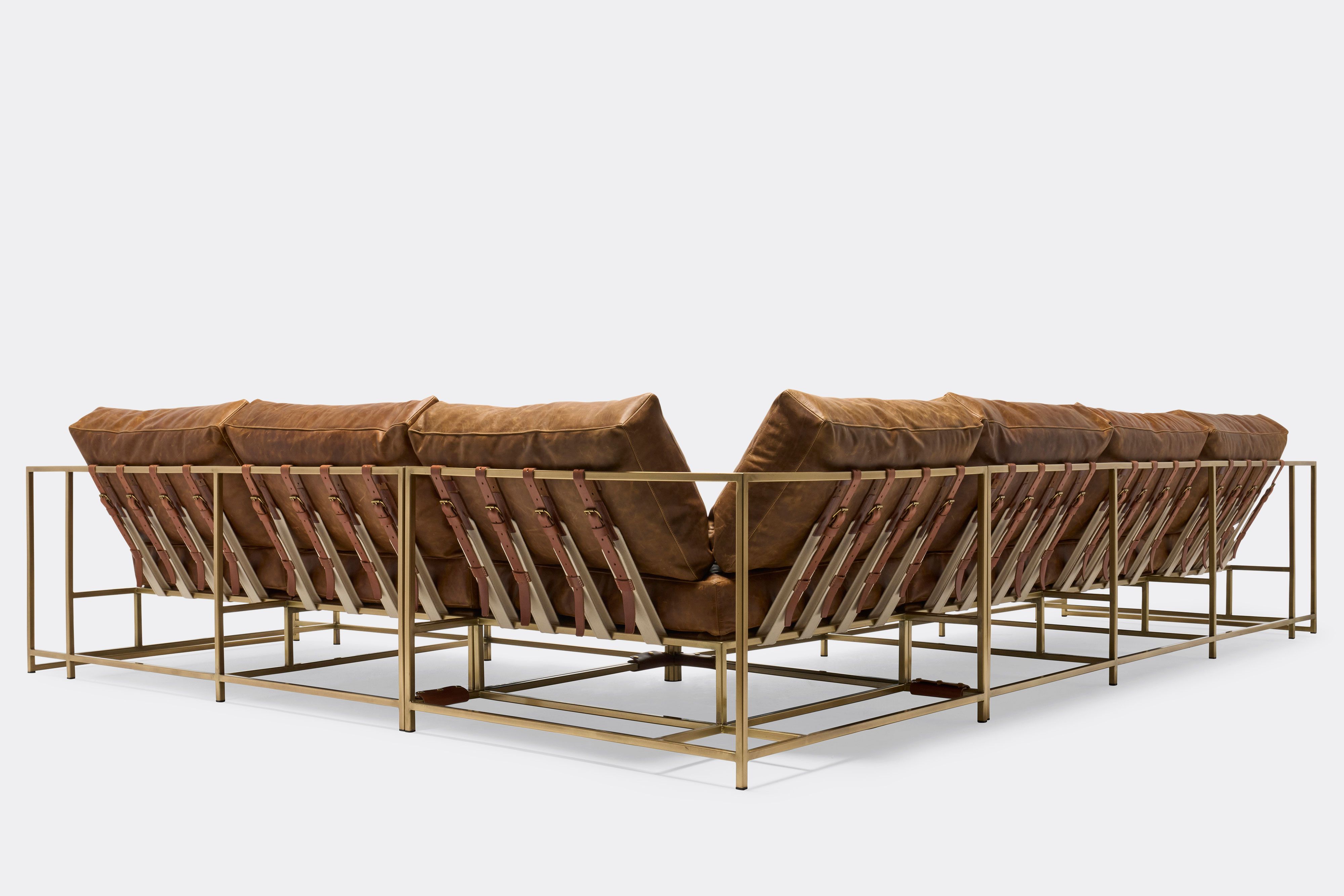 back of sectional with tan leather upholstery and brown leather belts on antique brass metal frame