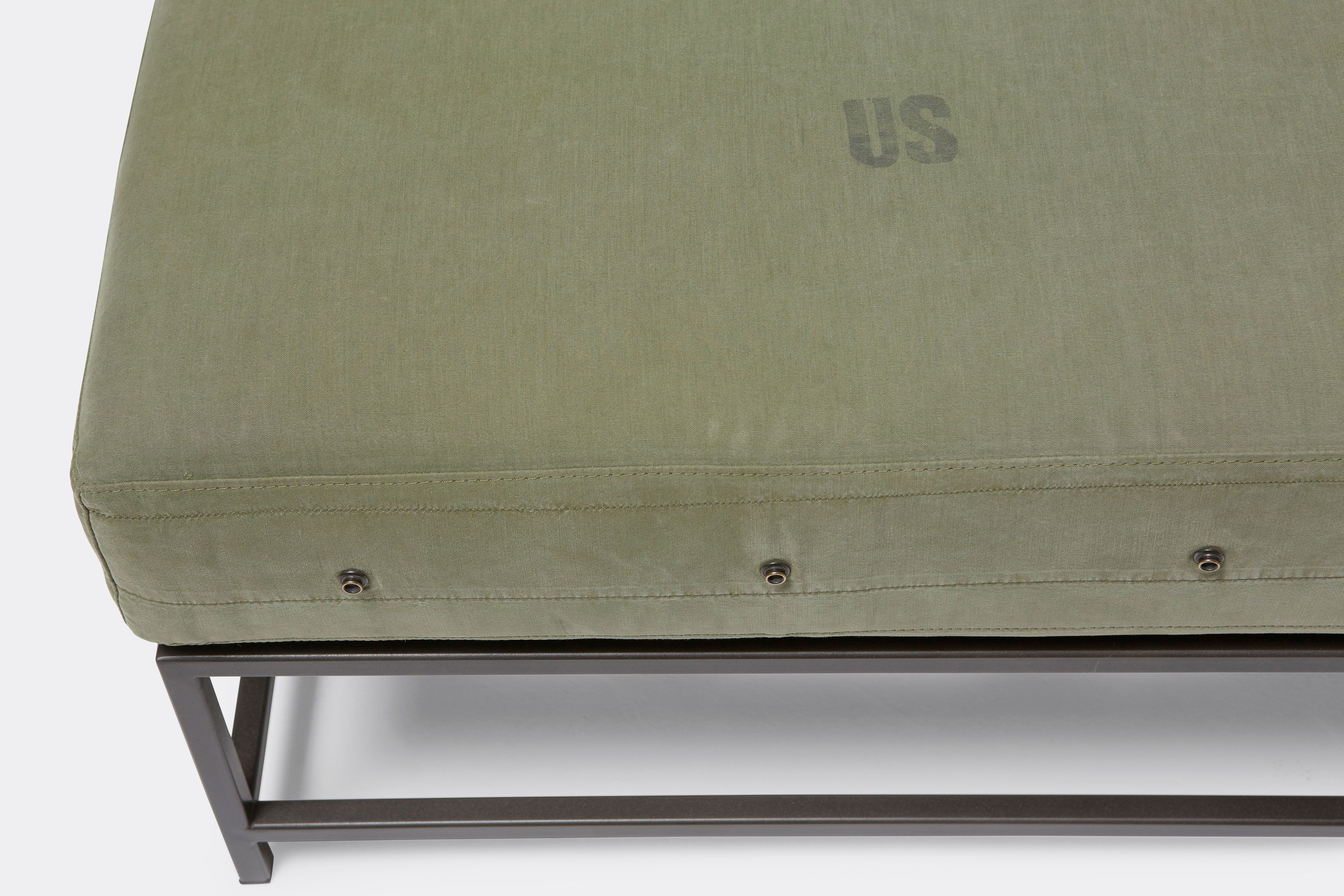 detail of bench with green canvas upholstery on black metal frame.