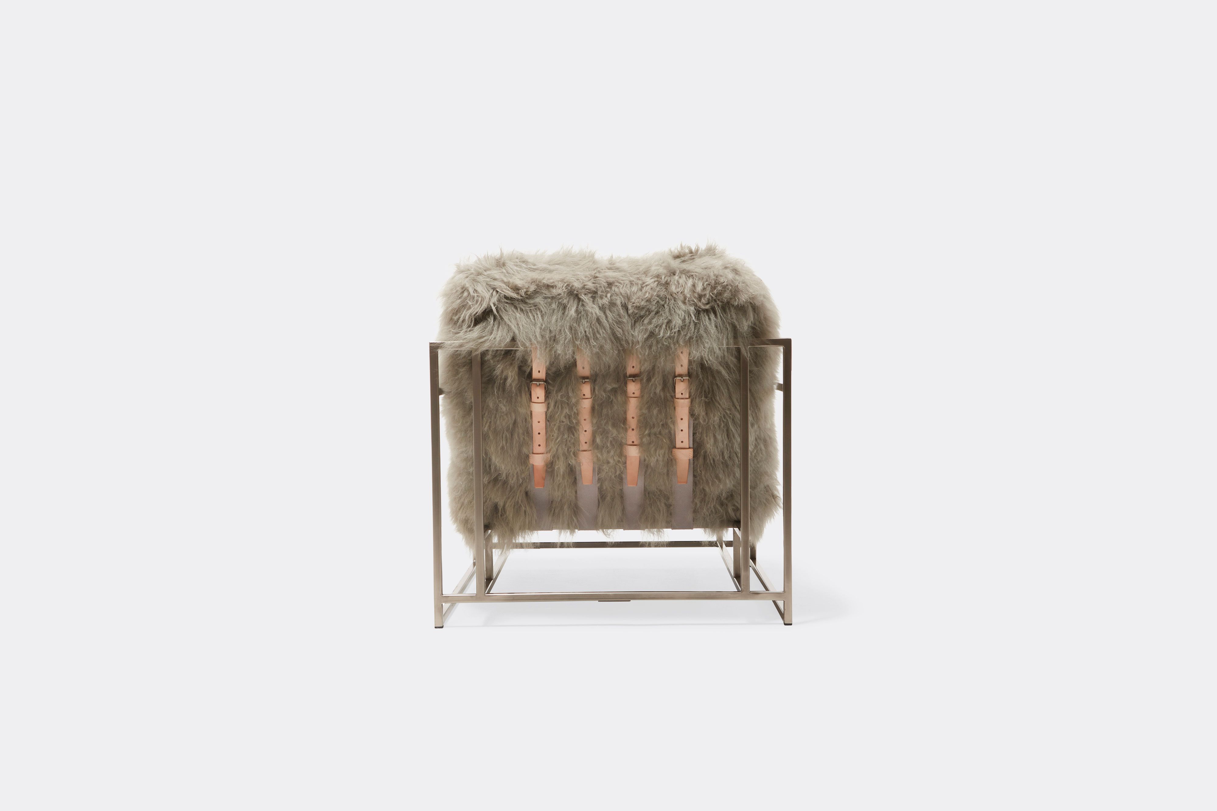 back of armchair with grey sheepskin upholstery and tan leather belts on antique nickel frame