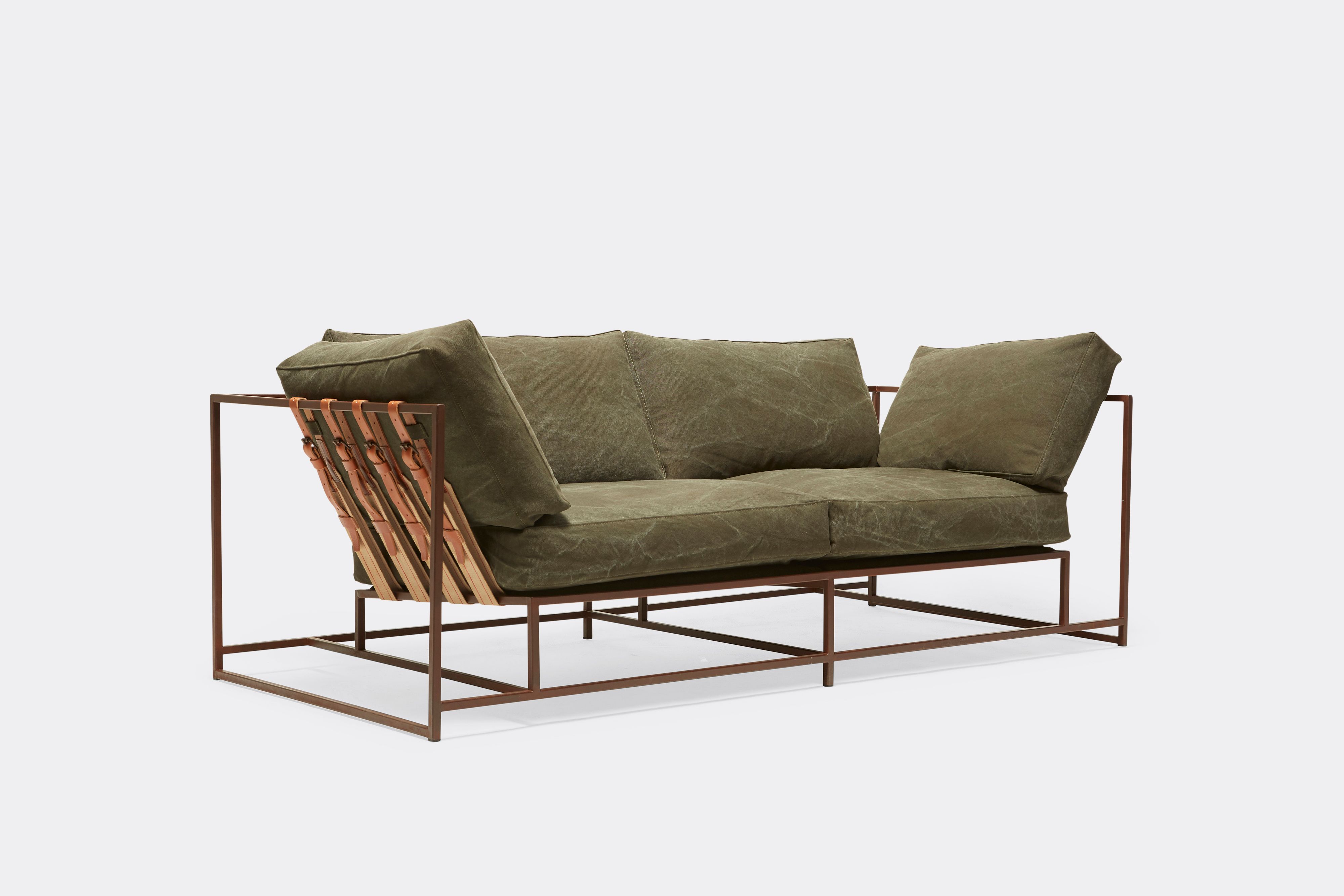 sideview of two seat sofa with olive canvas upholstery and brown leather belts on marbled rust metal frame