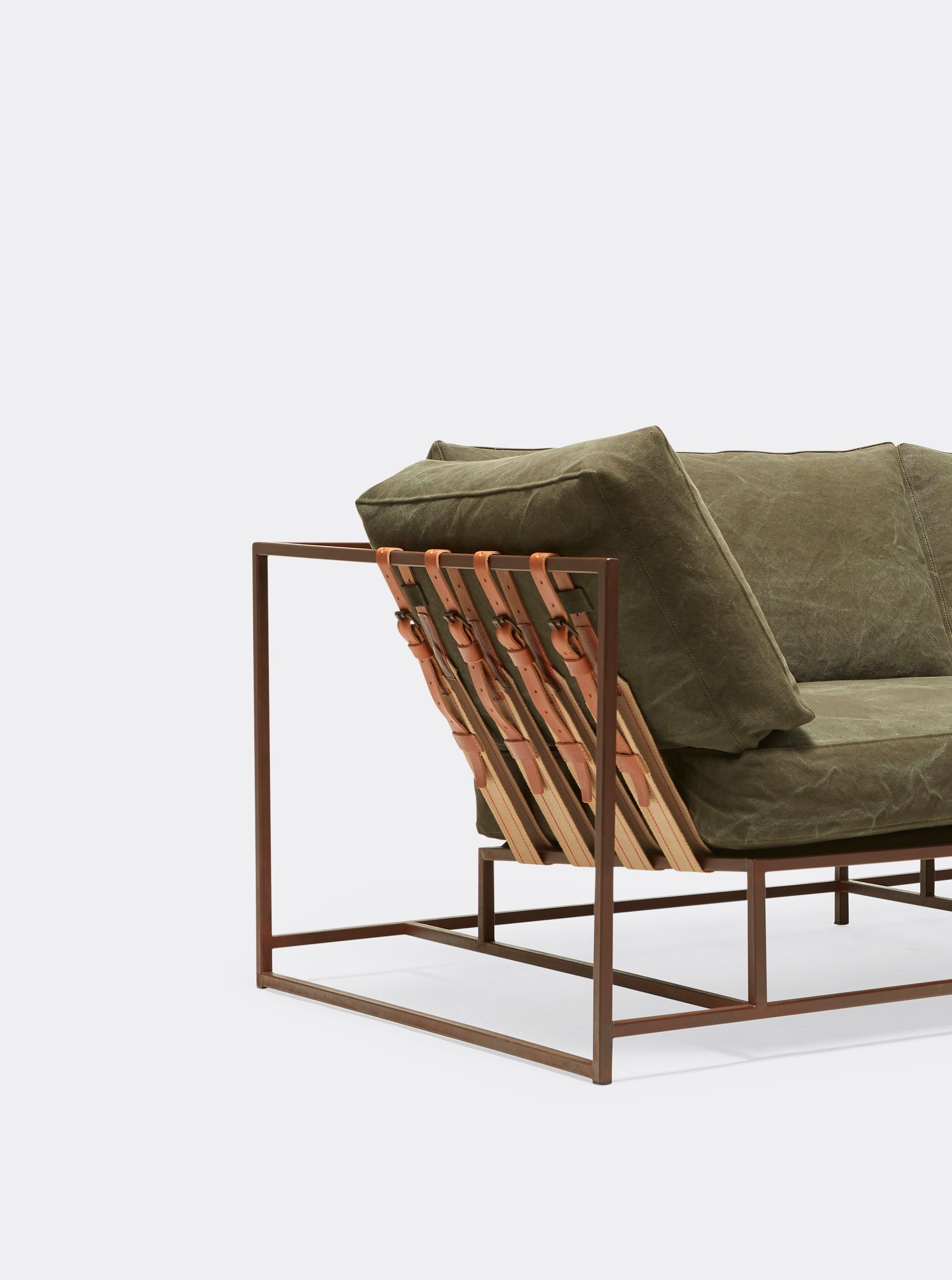 a green sofa with a rust finished steel frame and leather and webbing supporting belts on a white background .