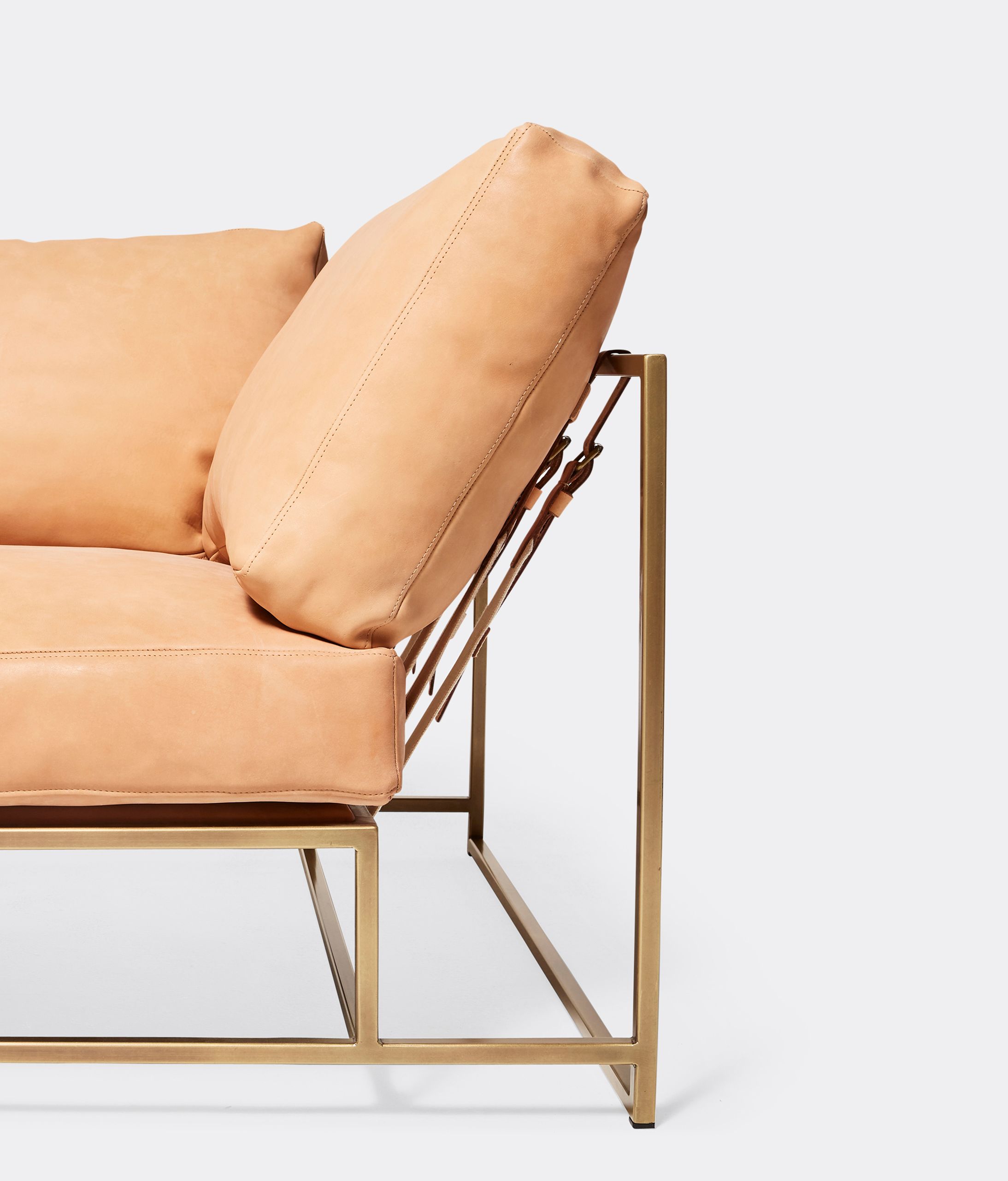 a tan leather couch with a brass frame and supporting belts shown on a white background .