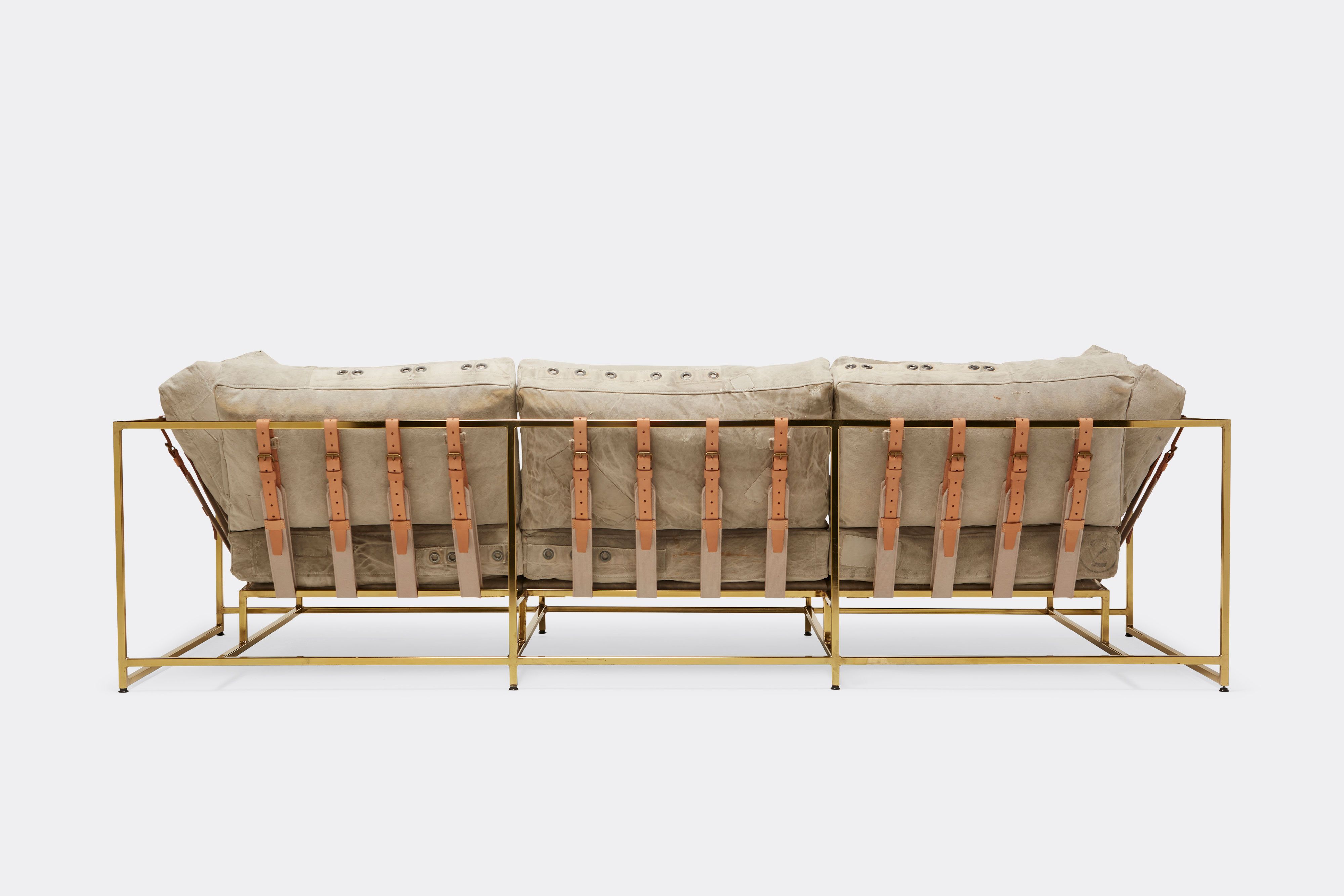 back of sofa with grey canvas upholstery and natural leather belts on polished brass metal frame