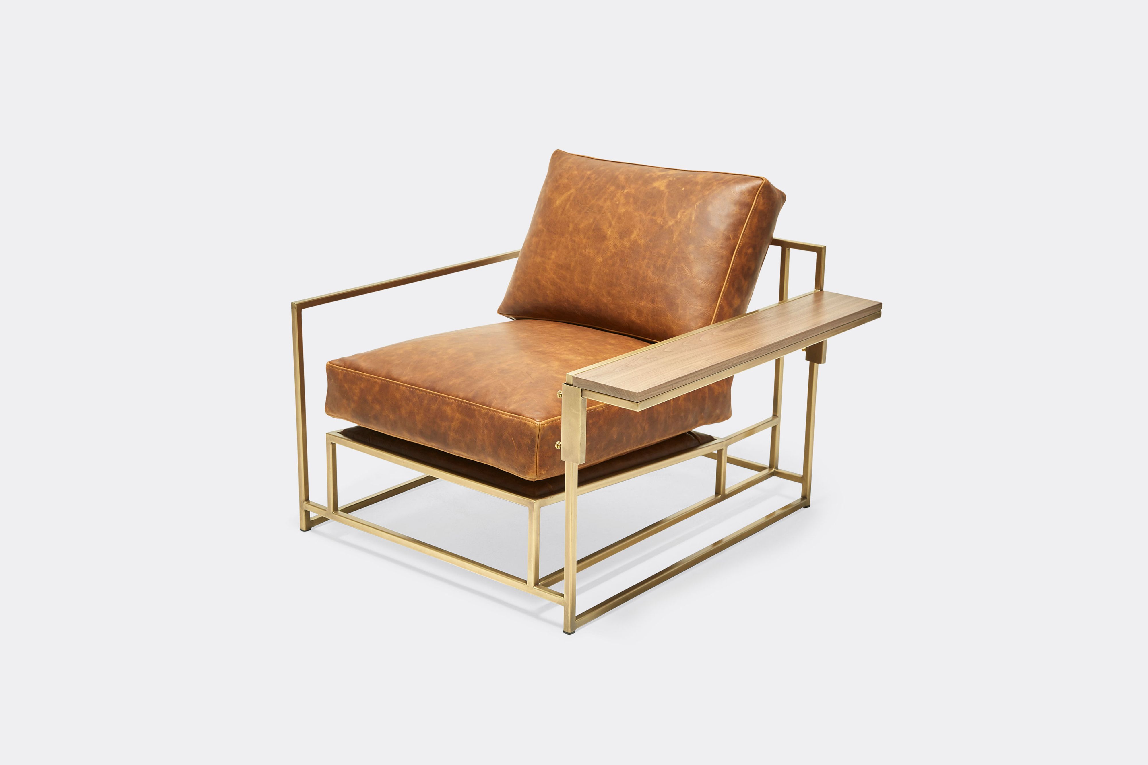 side of armchair and wing table with brown leather upholstery and brown leather belts on antique brass metal frame