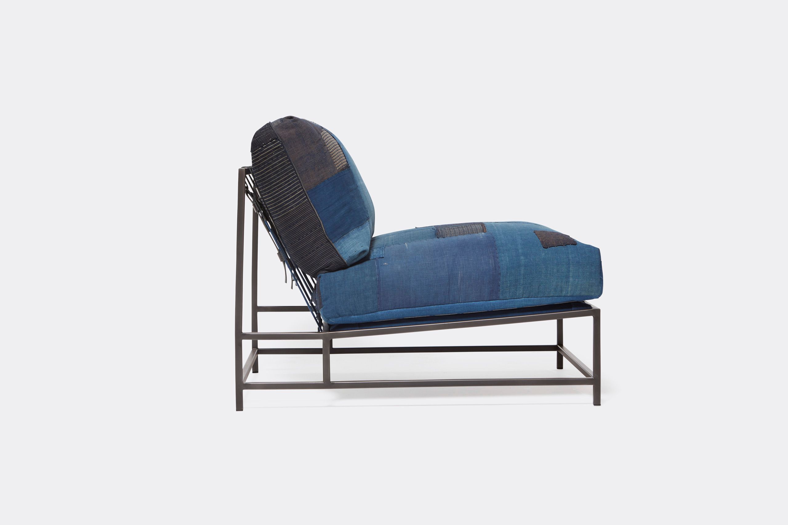 A steel framed chair upholstered with vintage japanese indigo and grey quilted material and blue and black supporting belts shown on a white background