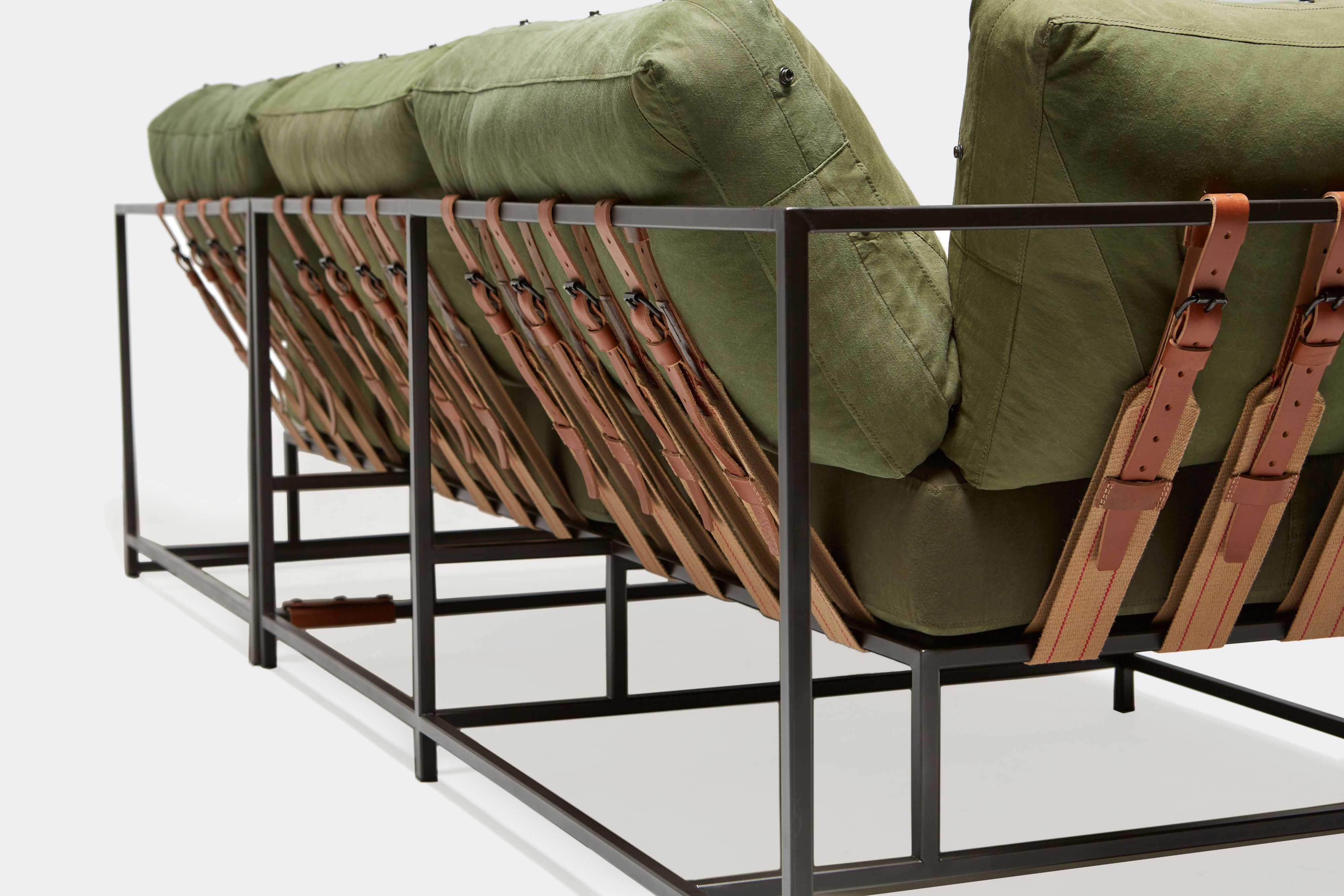 detail of sectional with green canvas upholstery and brown leather belts on black metal frame