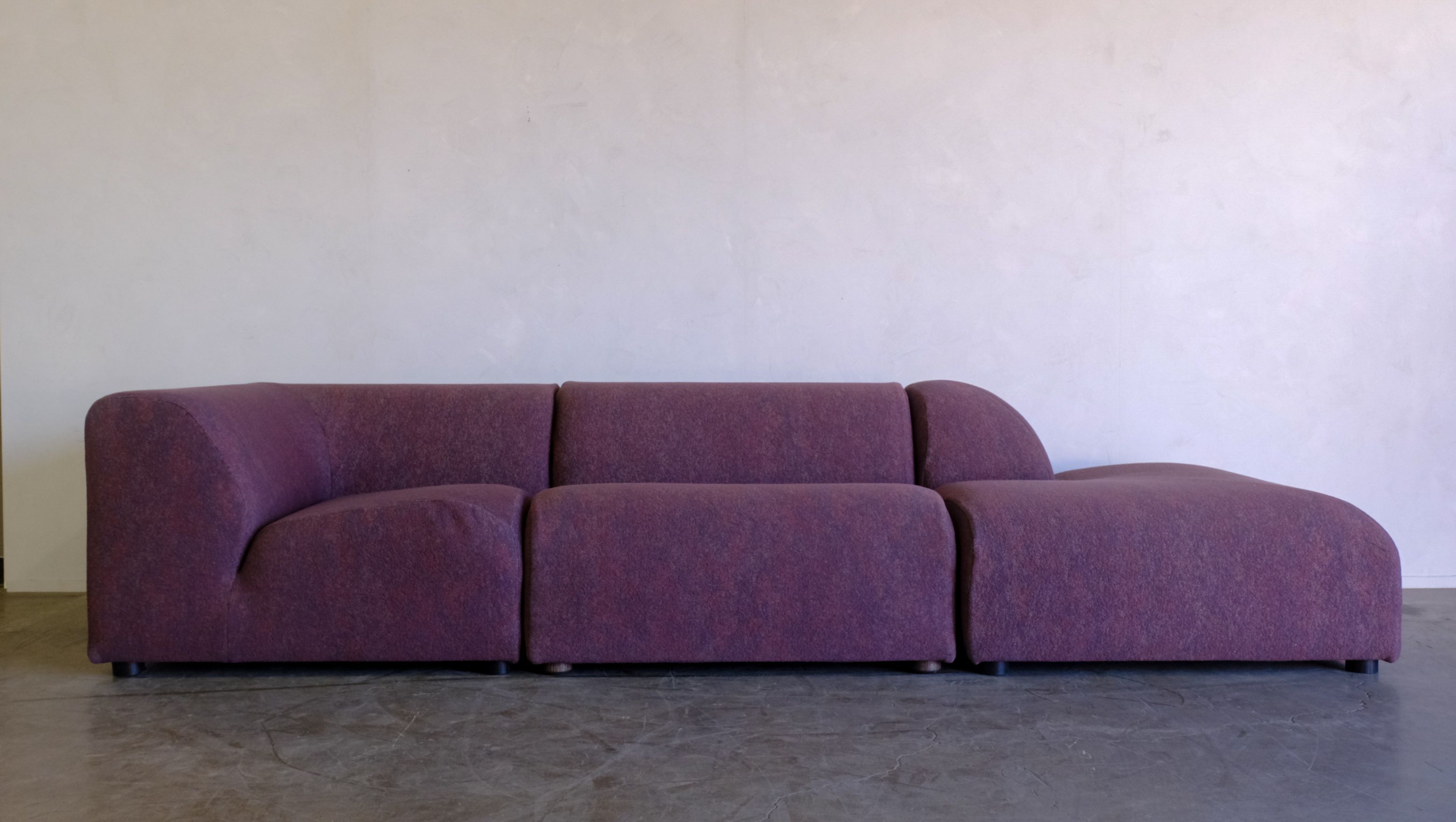 a purple couch is sitting on a concrete floor in front of a white wall .