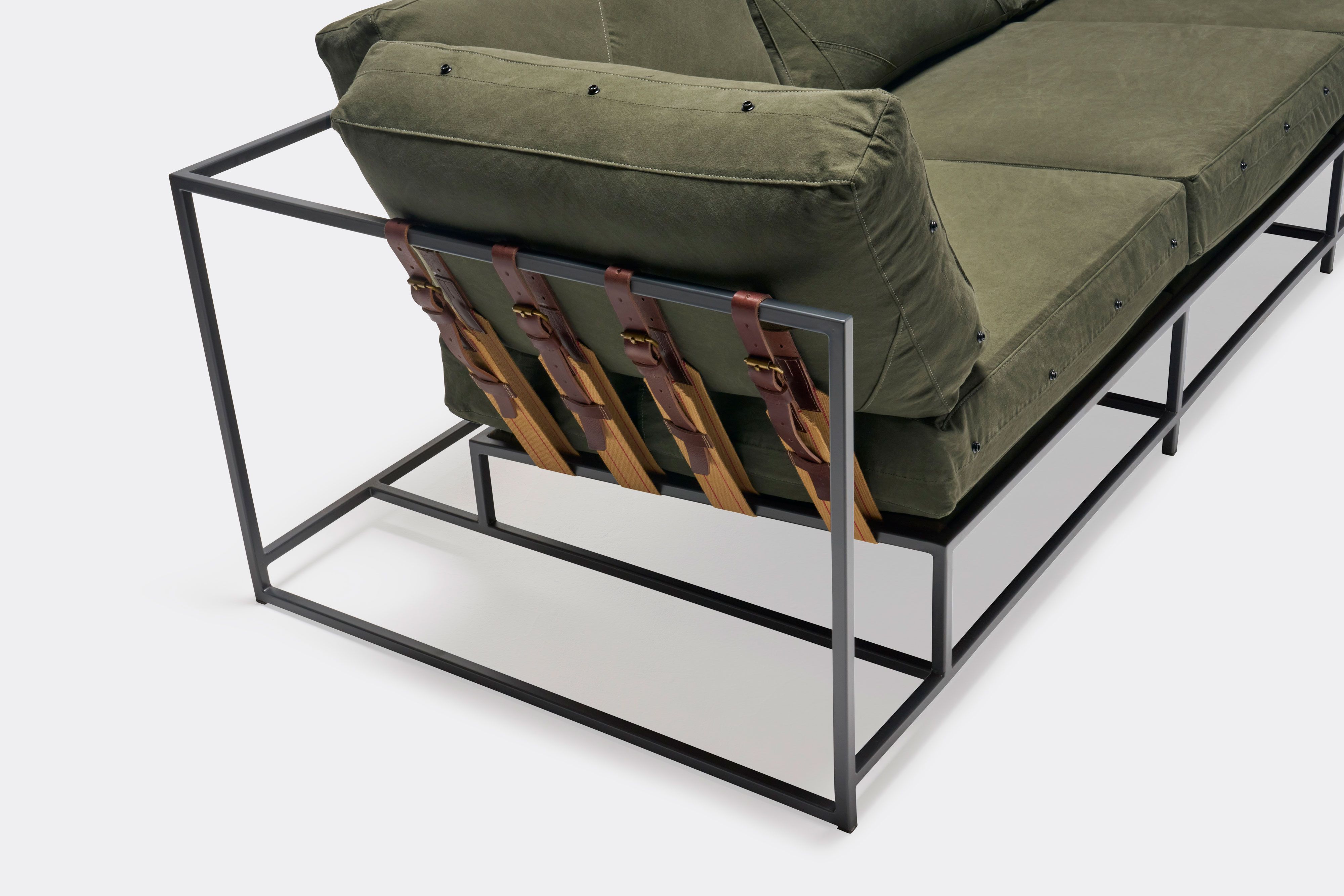 a green couch with a metal frame and leather straps