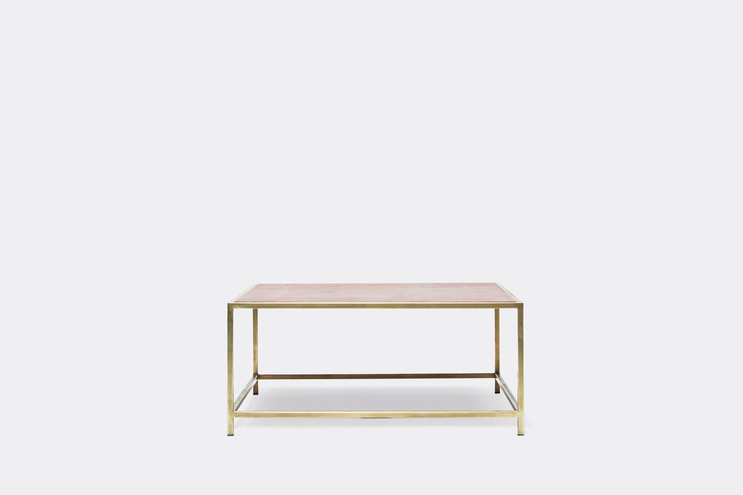 a square coffee table with a leather top and a brass frame on a white background .