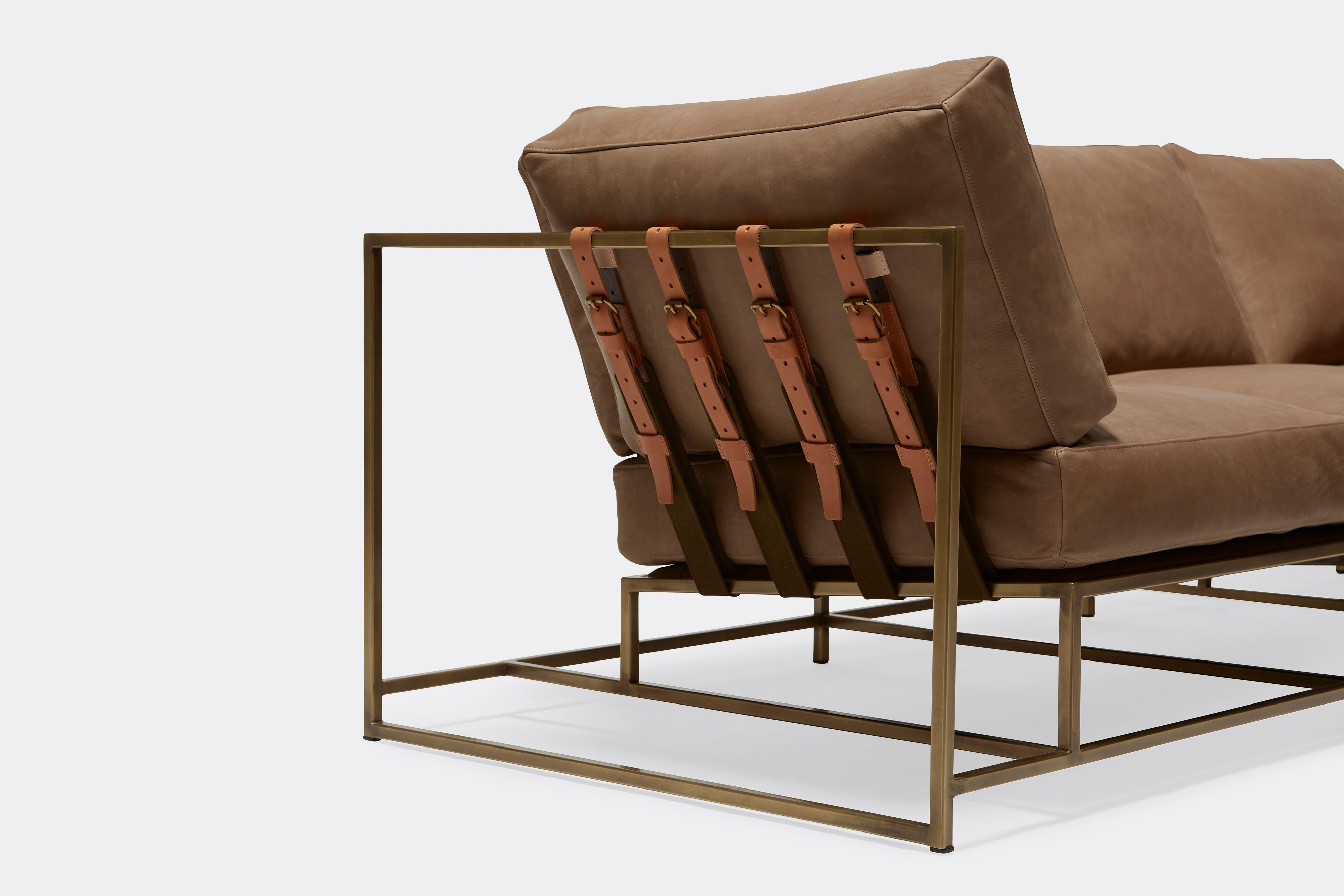 sideview of Sofa with brown leather upholstery and brown leather belts on antique brass metal frame