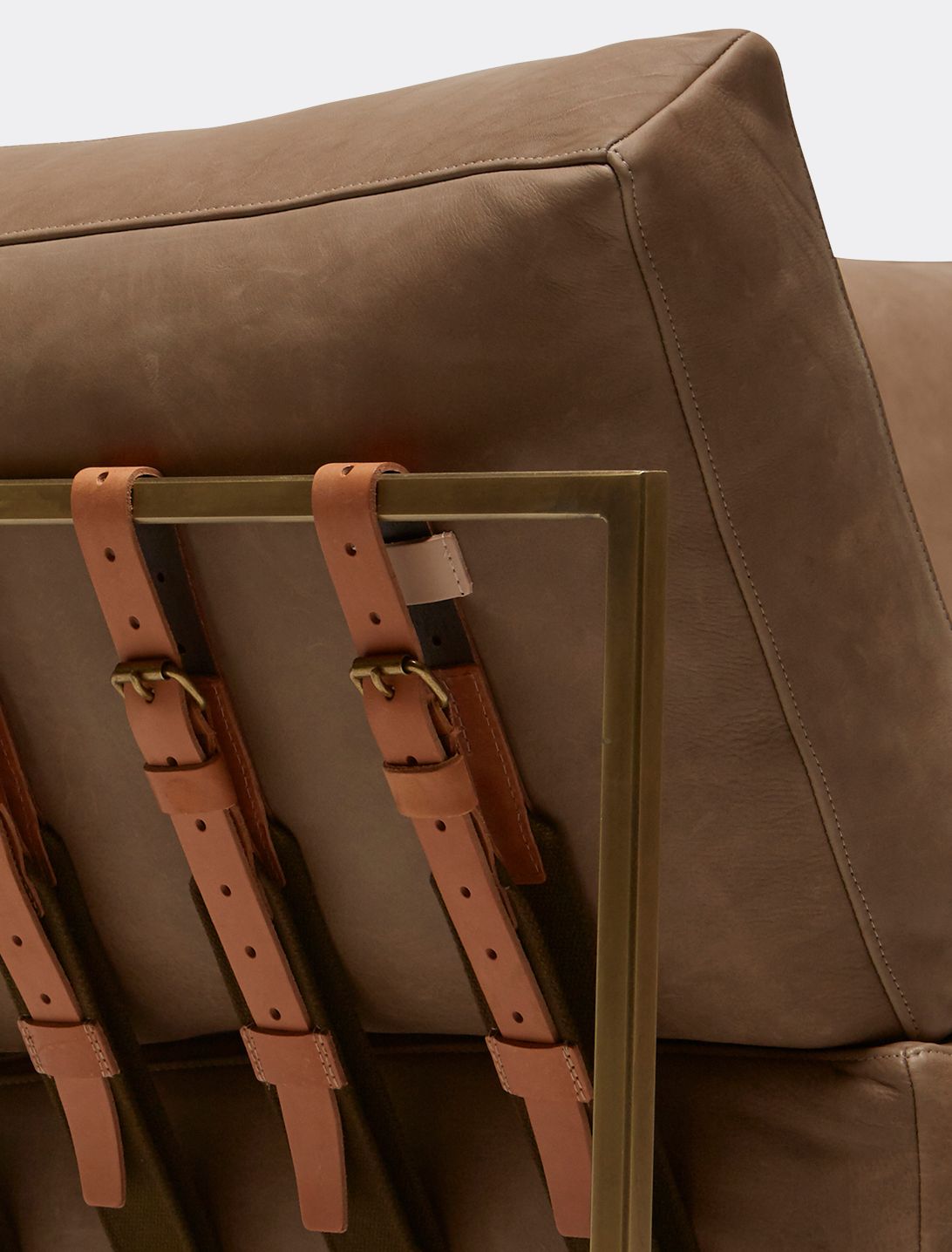  a brown leather couch with a brass metal frame and supporting belts shown on a white background .