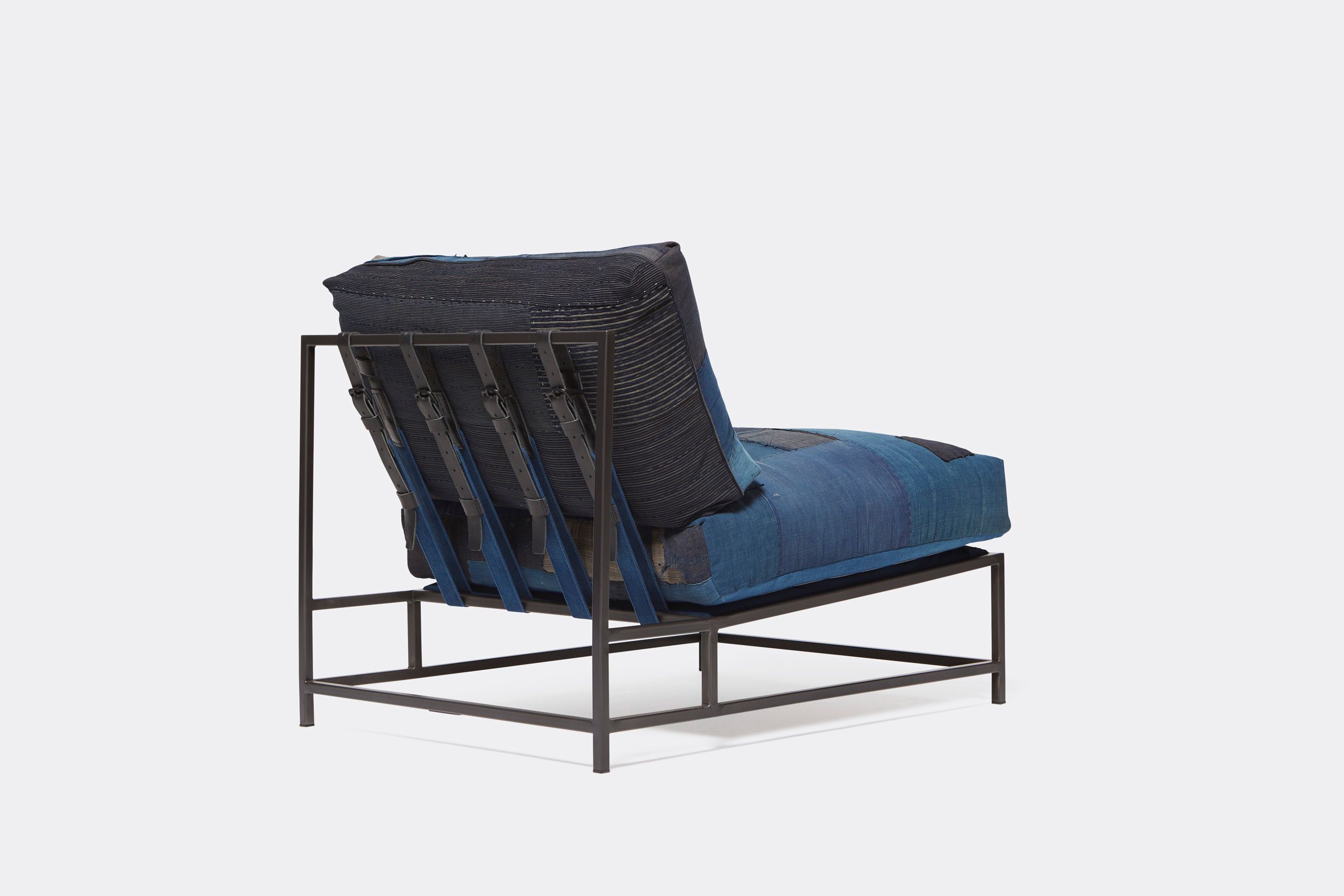 A steel framed chair upholstered with vintage japanese indigo and grey quilted material and blue and black supporting belts shown on a white background