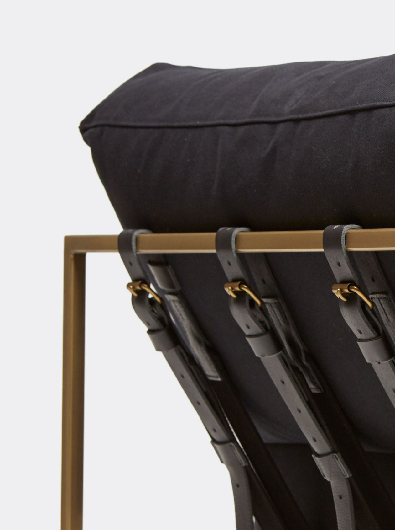 a black wool upholstered chaise with a brass metal frame and black supporting belts shown on a white background .