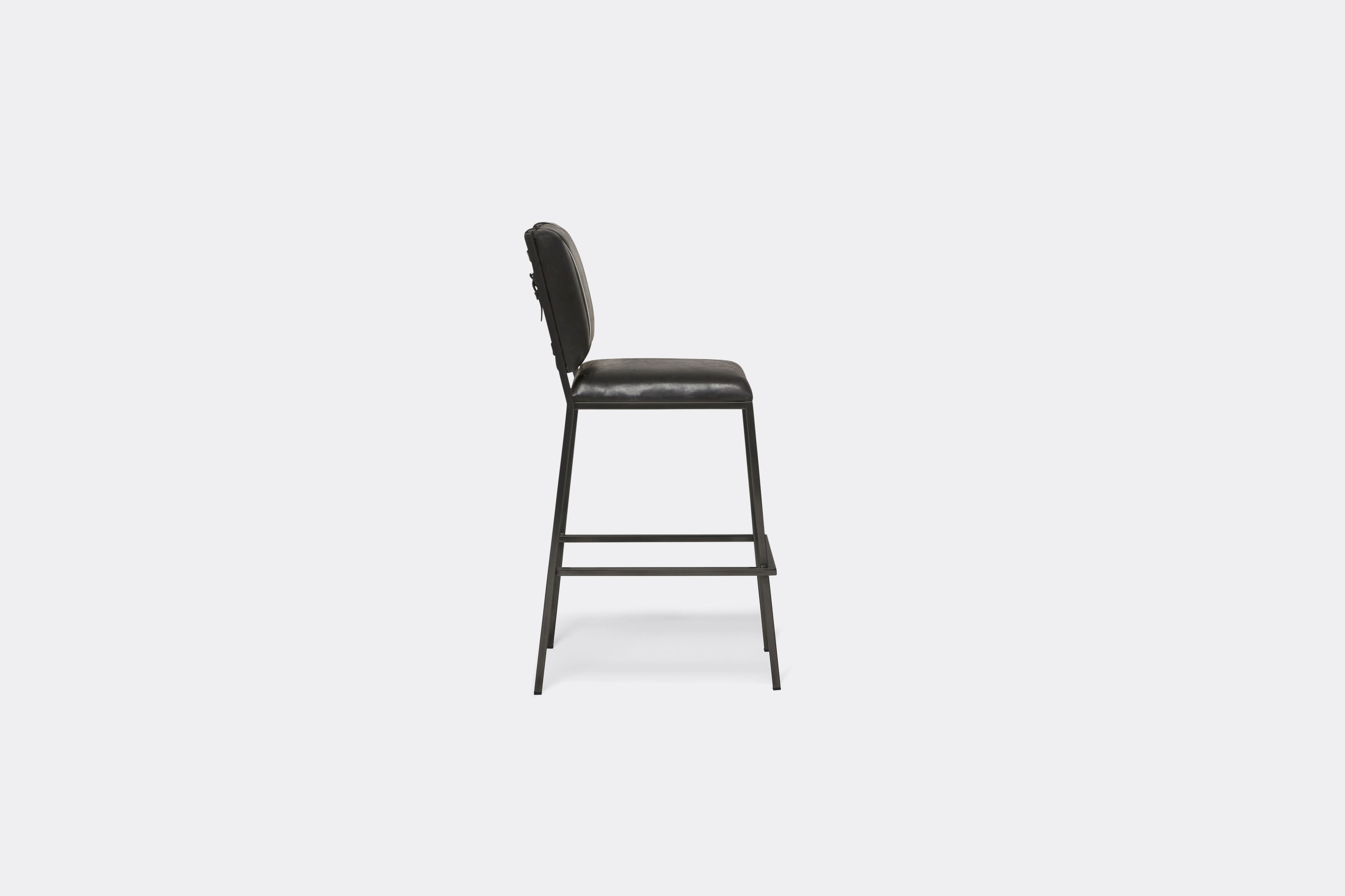 Sideview of barstool with black leather upholstery and black leather belts on blackened steel metal legs