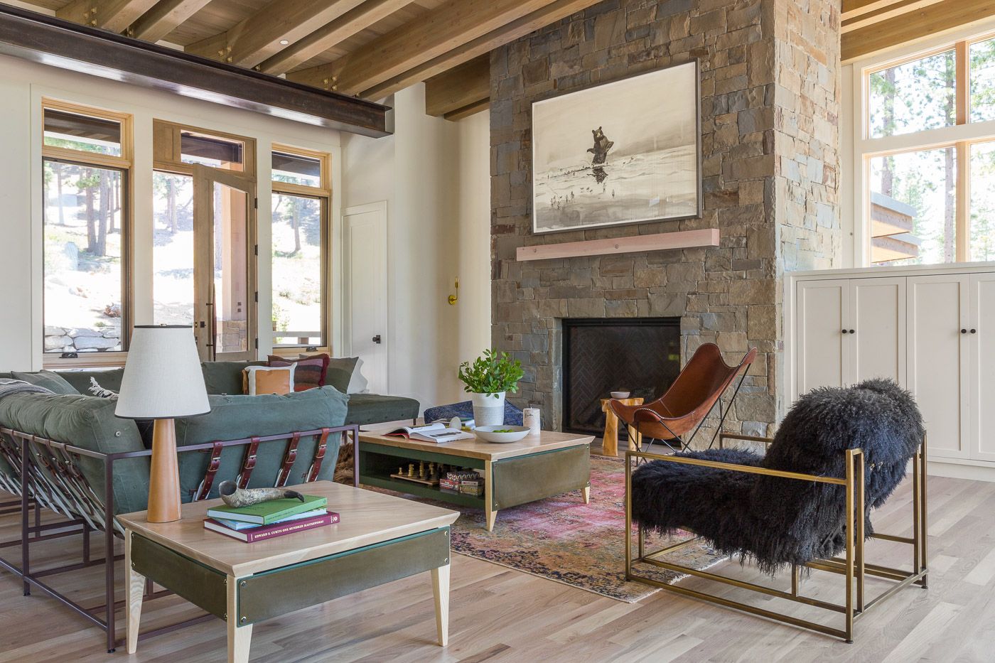 a living room filled with furniture on a wood floor and a large stone fireplace next to big windows with trees outside