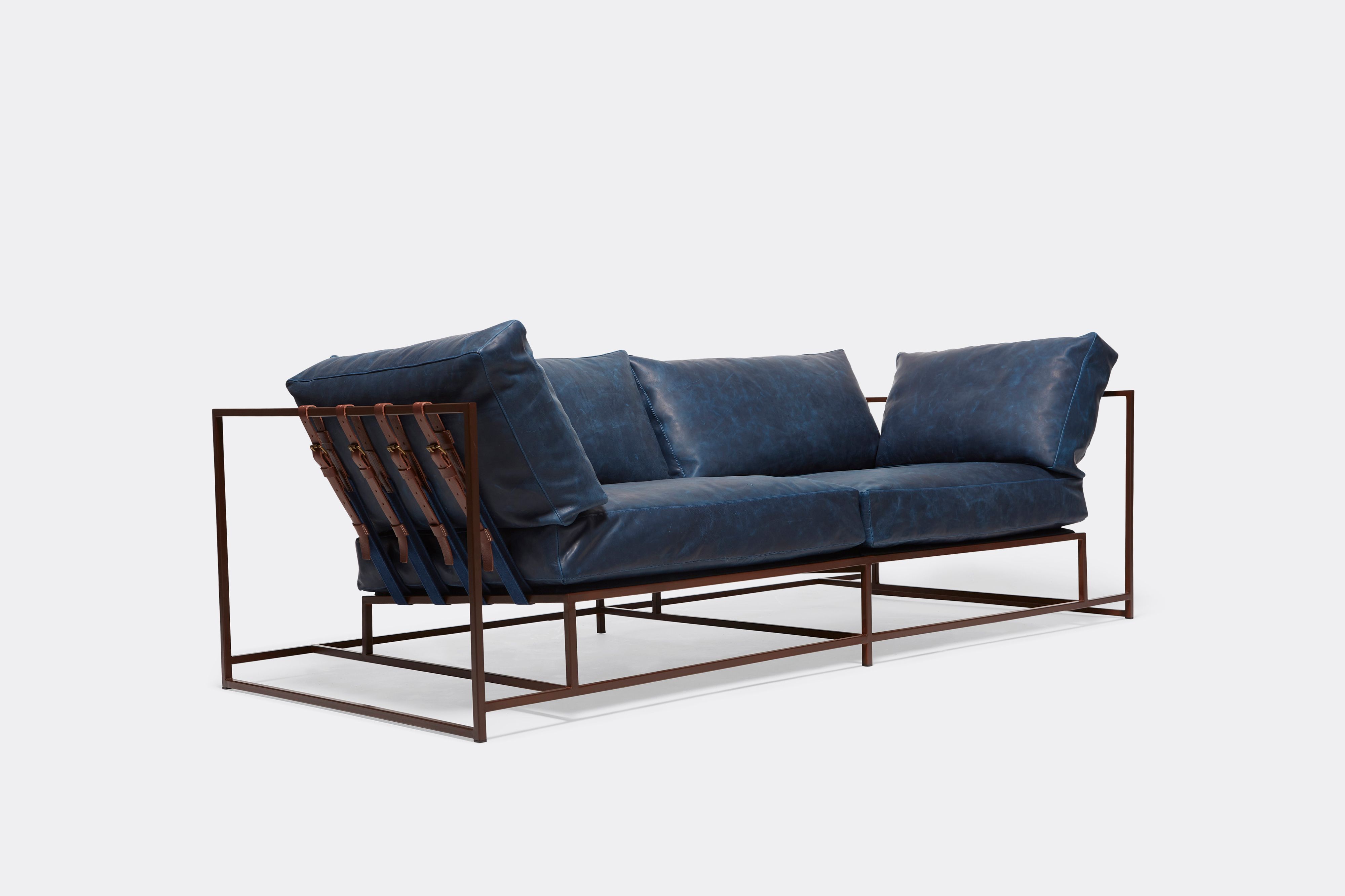 Side of two seat sofa with blue leather upholstery and brown leather belts on marble rust metal frame