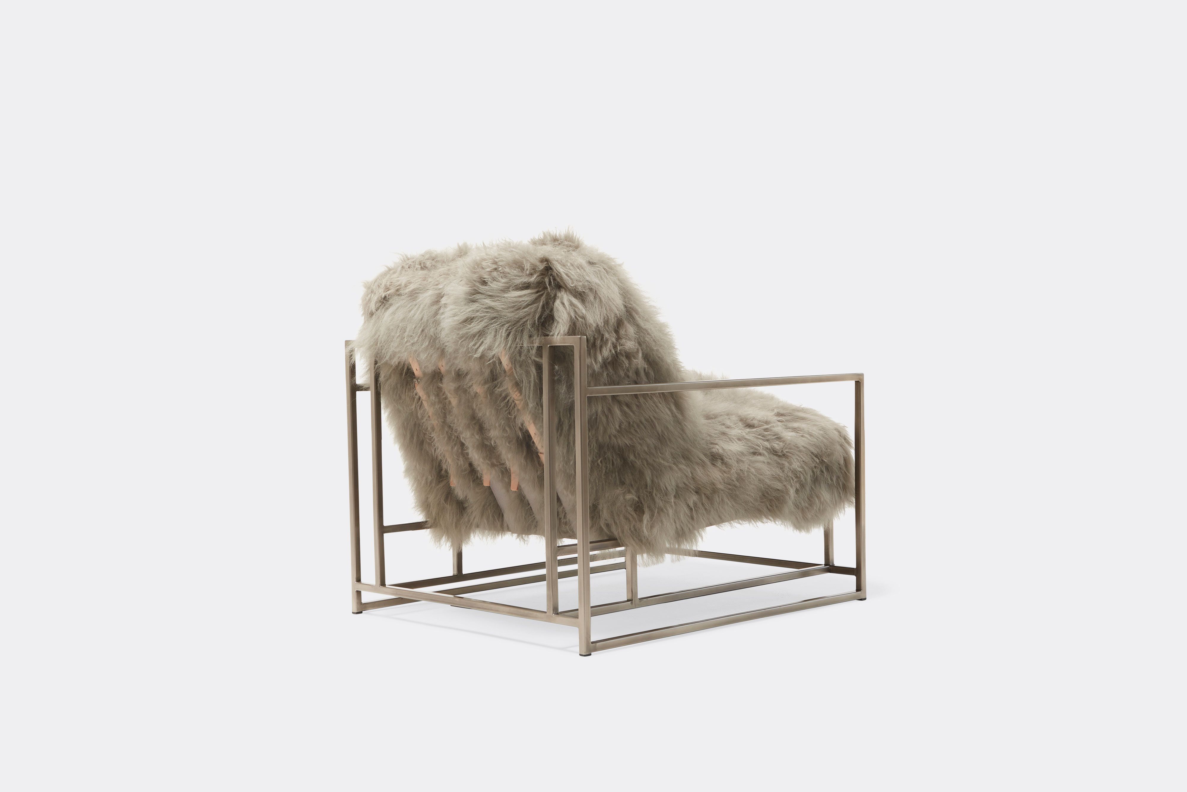 back of armchair with grey sheepskin upholstery and tan leather belts on antique nickel frame
