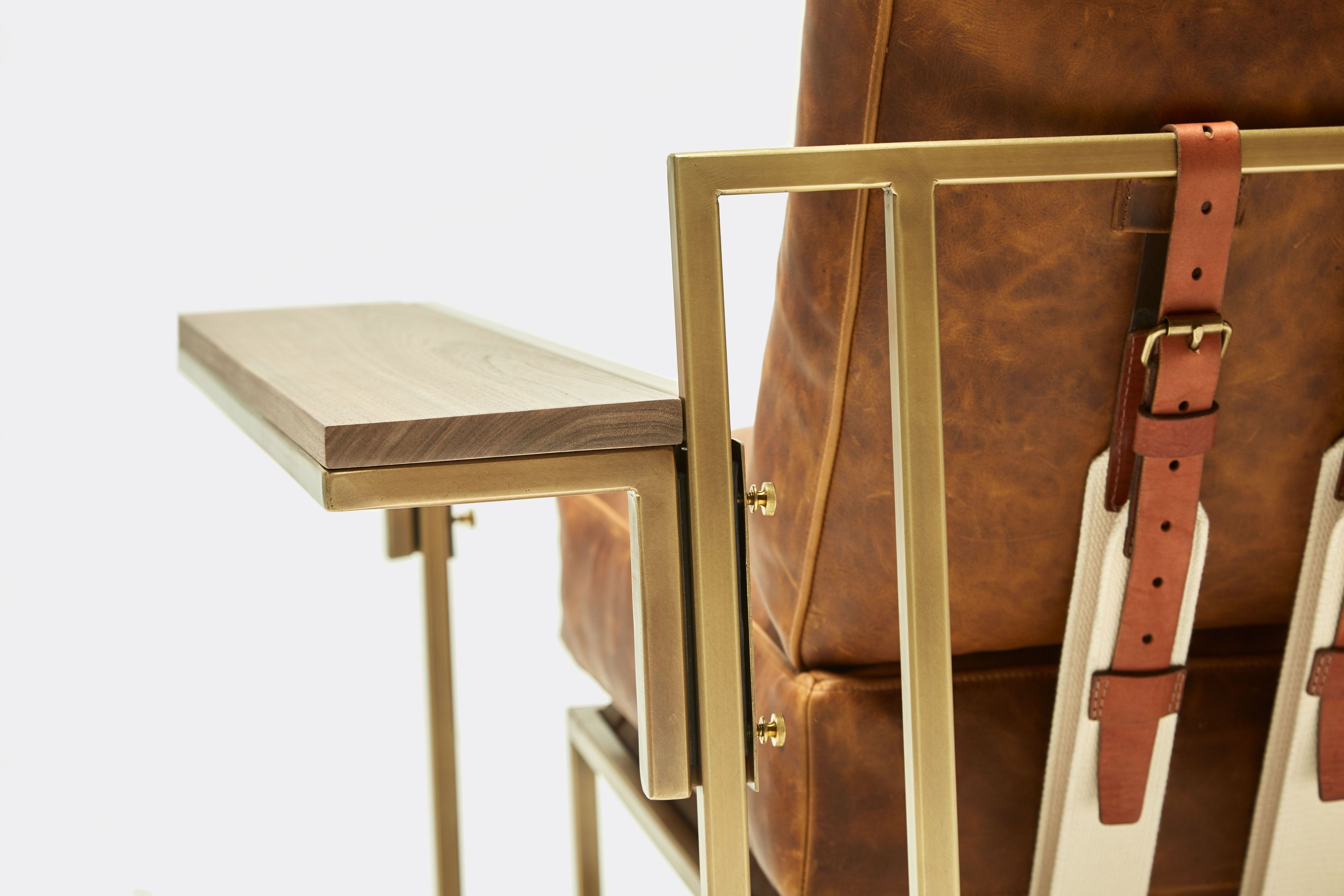 back of armchair with brown leather upholstery and brown leather belts on antique brass metal frame with wing table