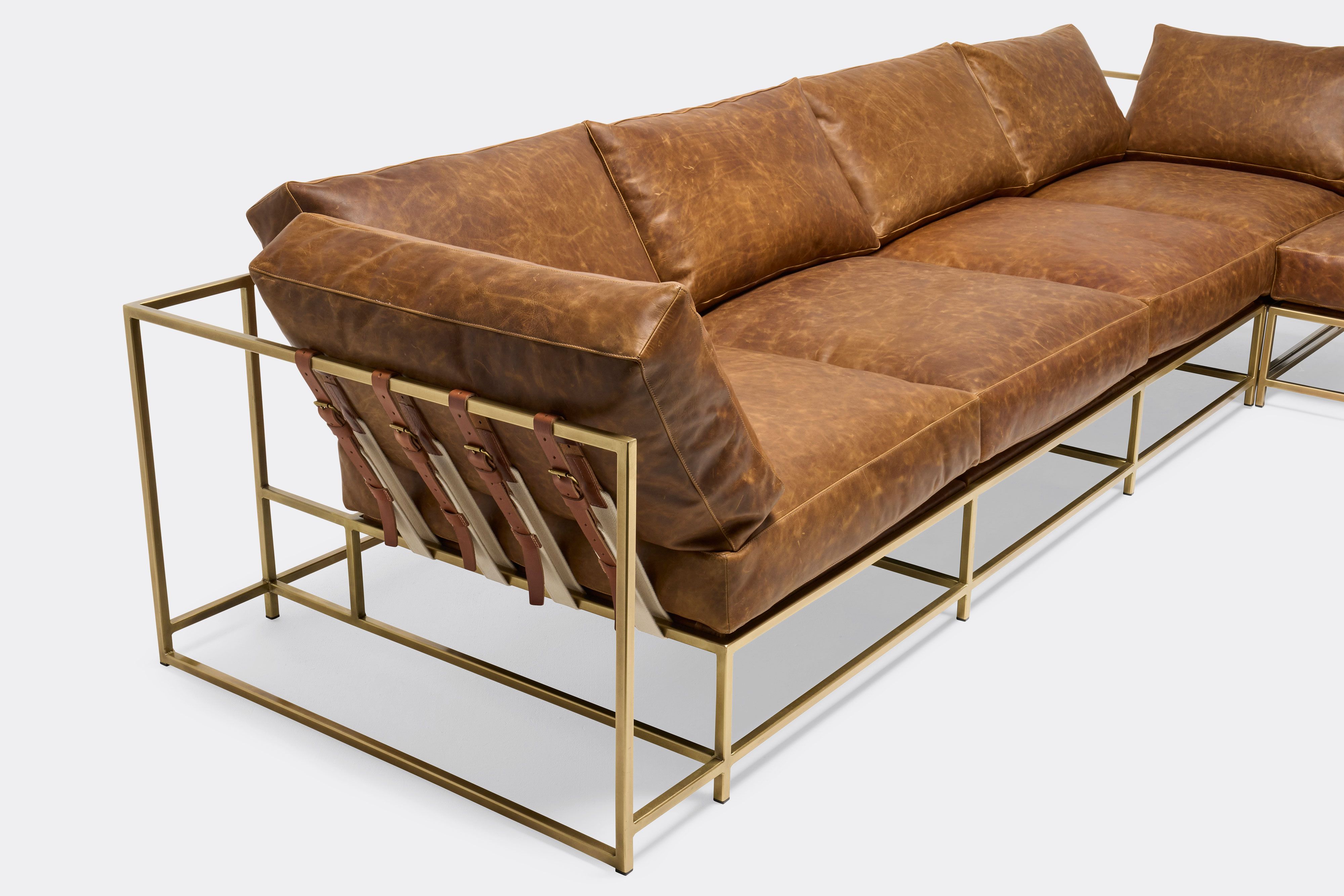 overhead detail of sectional with tan leather upholstery and brown leather belts on antique brass metal frame