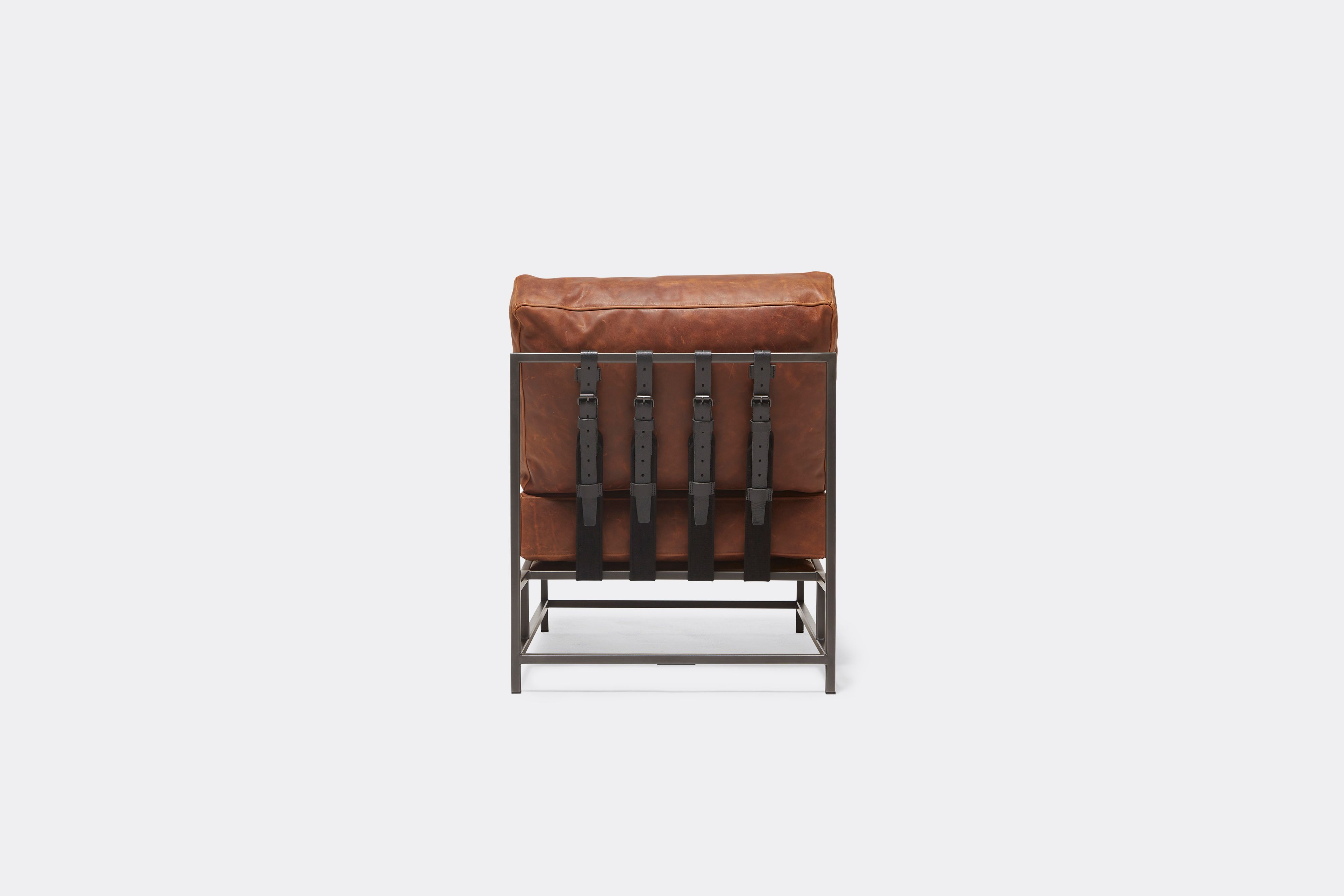 A brown leather chair with black leather and webbing belts and a blackened steel frame shown on a white background