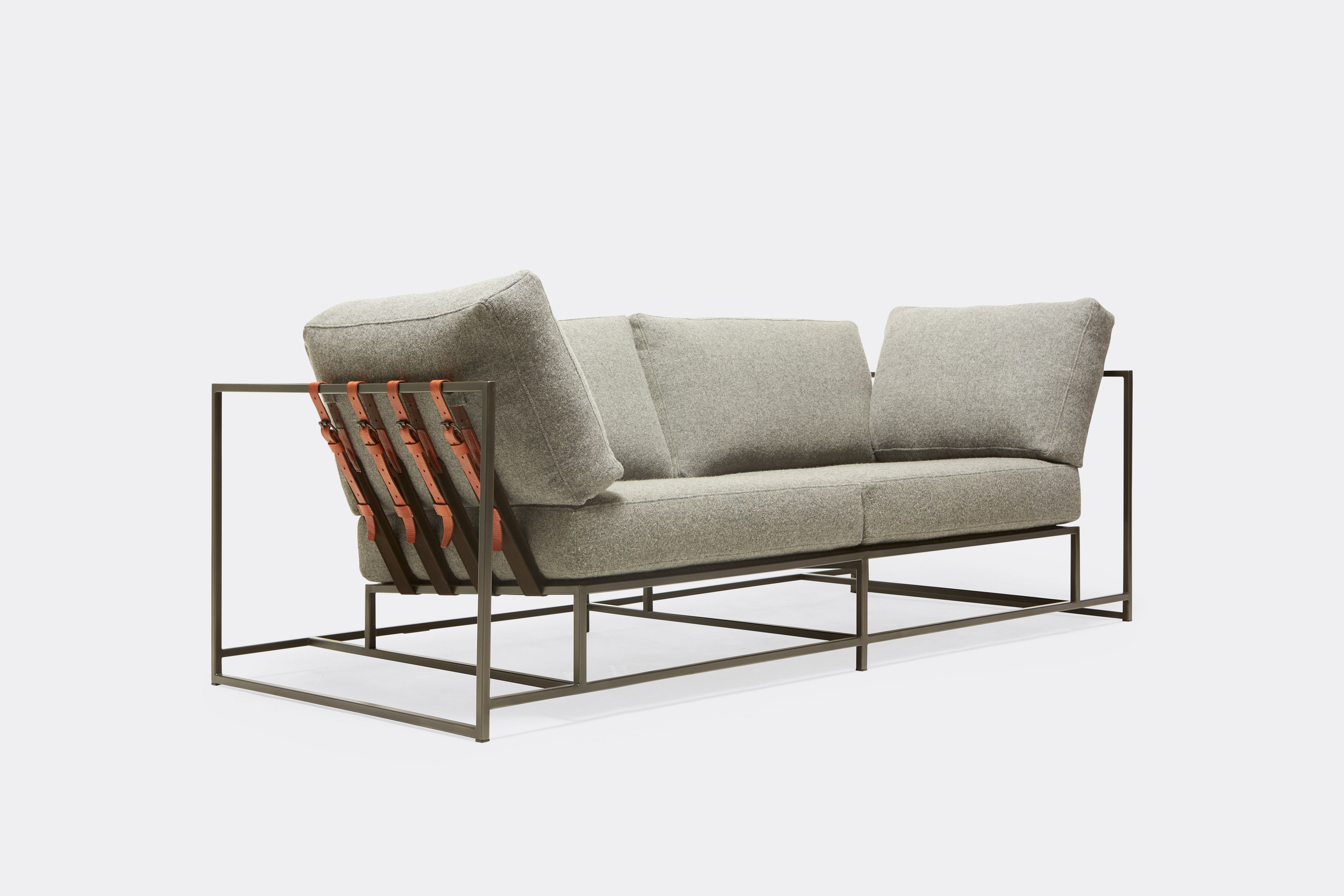 sideview of two seat sofa with grey wool upholstery and brown leather belts on black metal frame