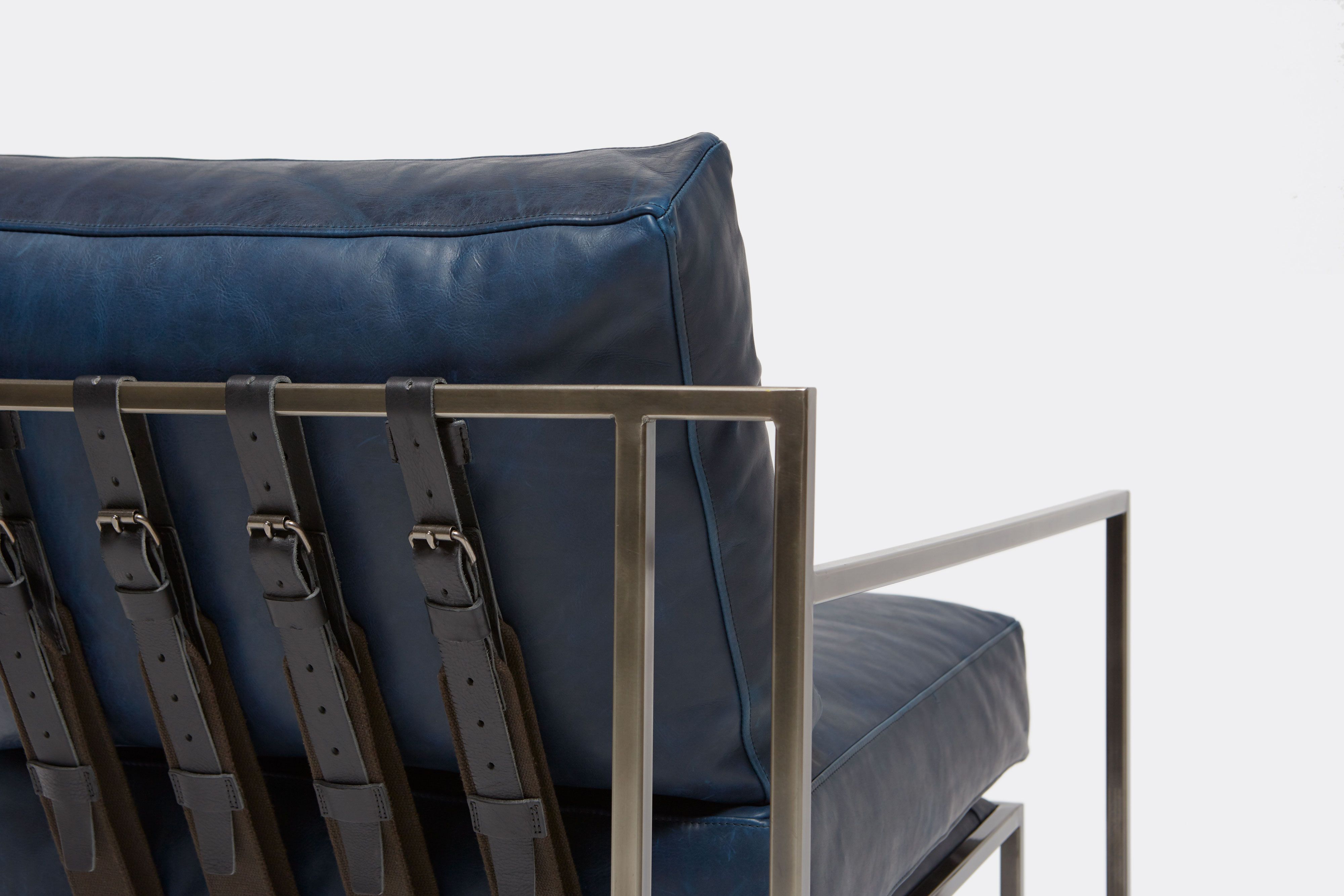back detail of armchair with blue leather upholstery and black leather belts on antique nickel metal frame