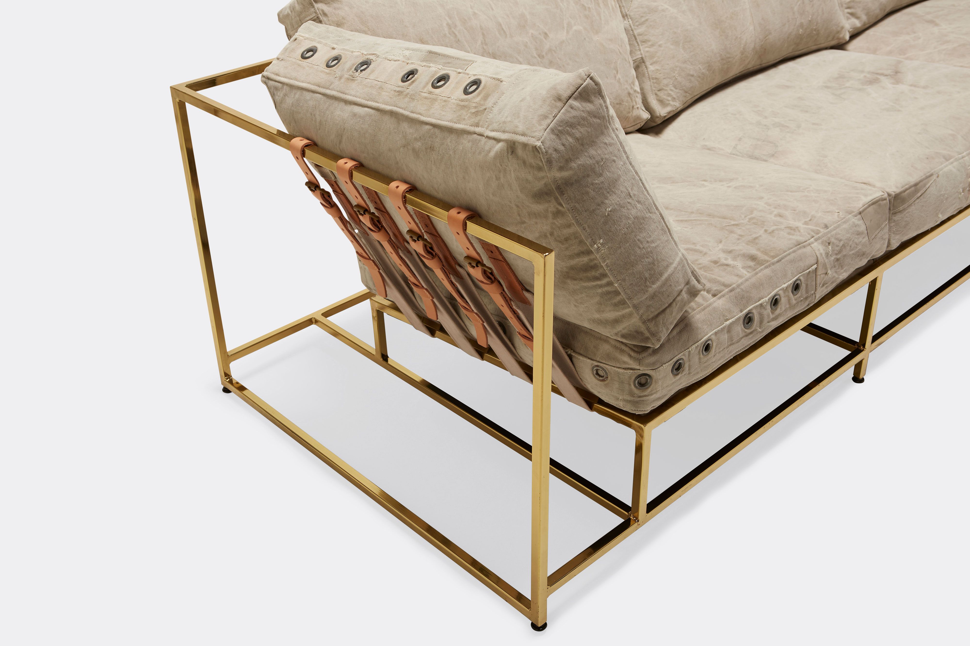 overhead detail of sofa with grey canvas upholstery and natural leather belts on polished brass metal frame