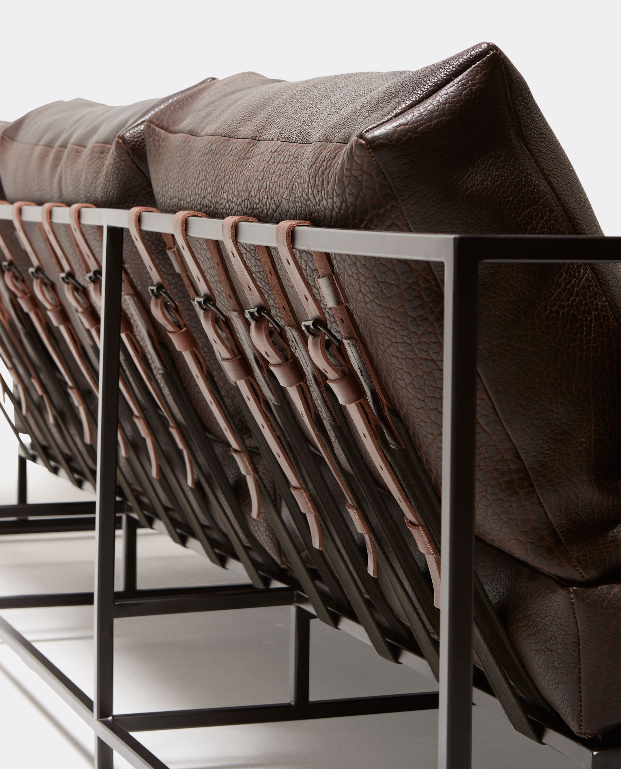 a textured brown leather couch with a metal frame and leather and webbing supporting belts shown on a white background.