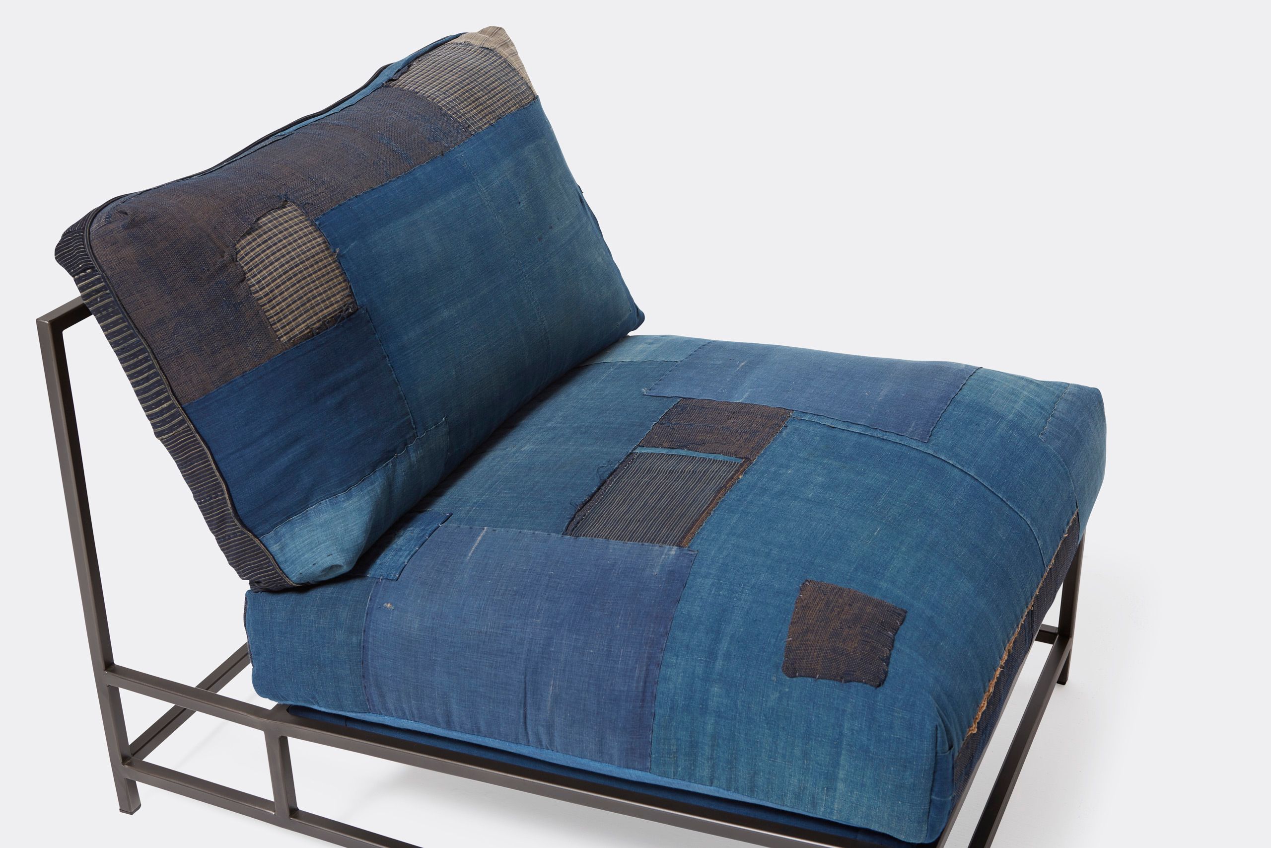 A steel framed chair upholstered with vintage japanese indigo and grey quilted material and blue and black supporting belts shown on a white background