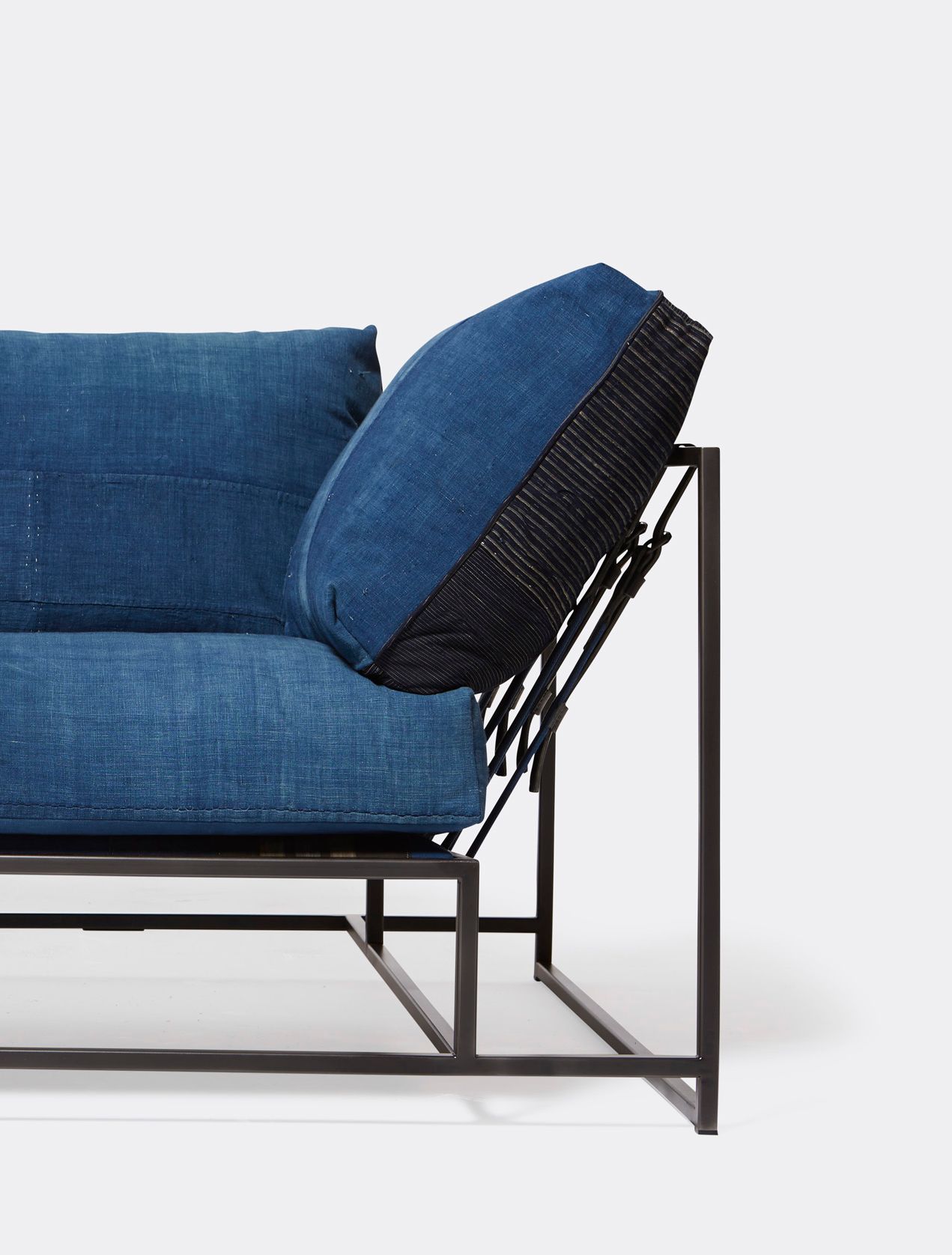 A steel framed sofa with vintage Japanese indigo and grey upholstery and supporting belts shown on a white background
