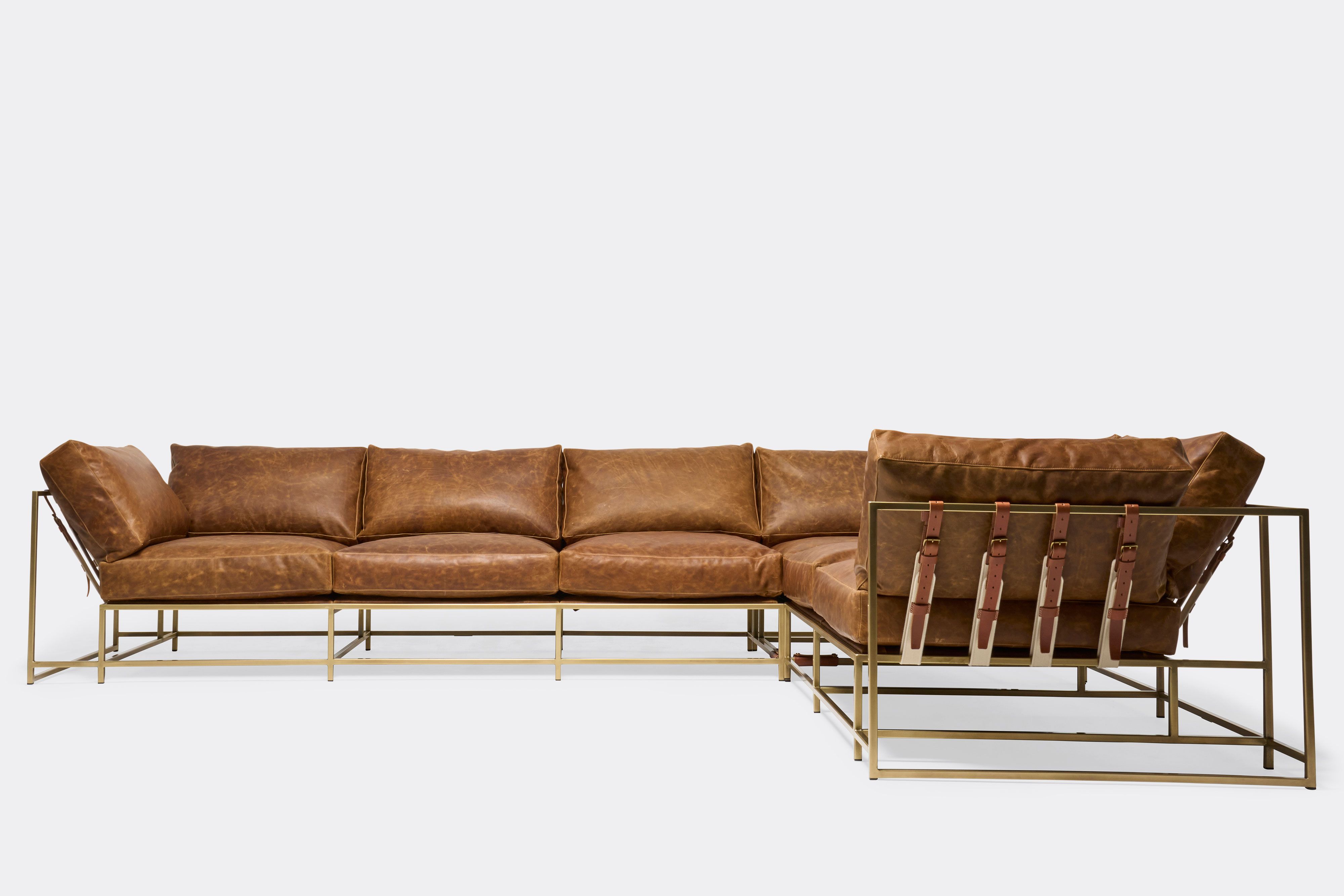 front with side of sectional with tan leather upholstery and brown leather belts on antique brass metal frame