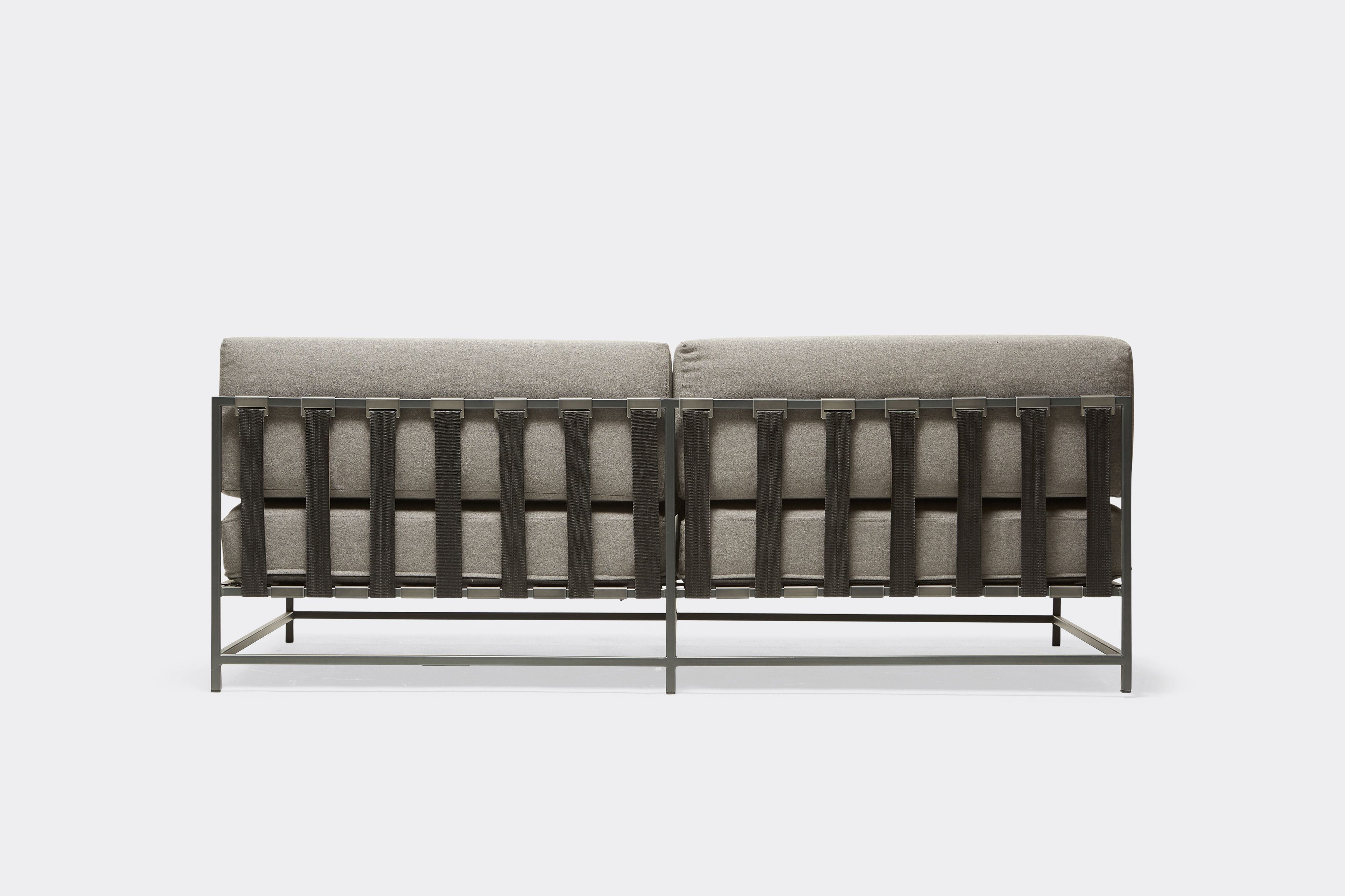 back of outdoor loveseat with grey canvas upholstery and black belts on charcoal metal frame