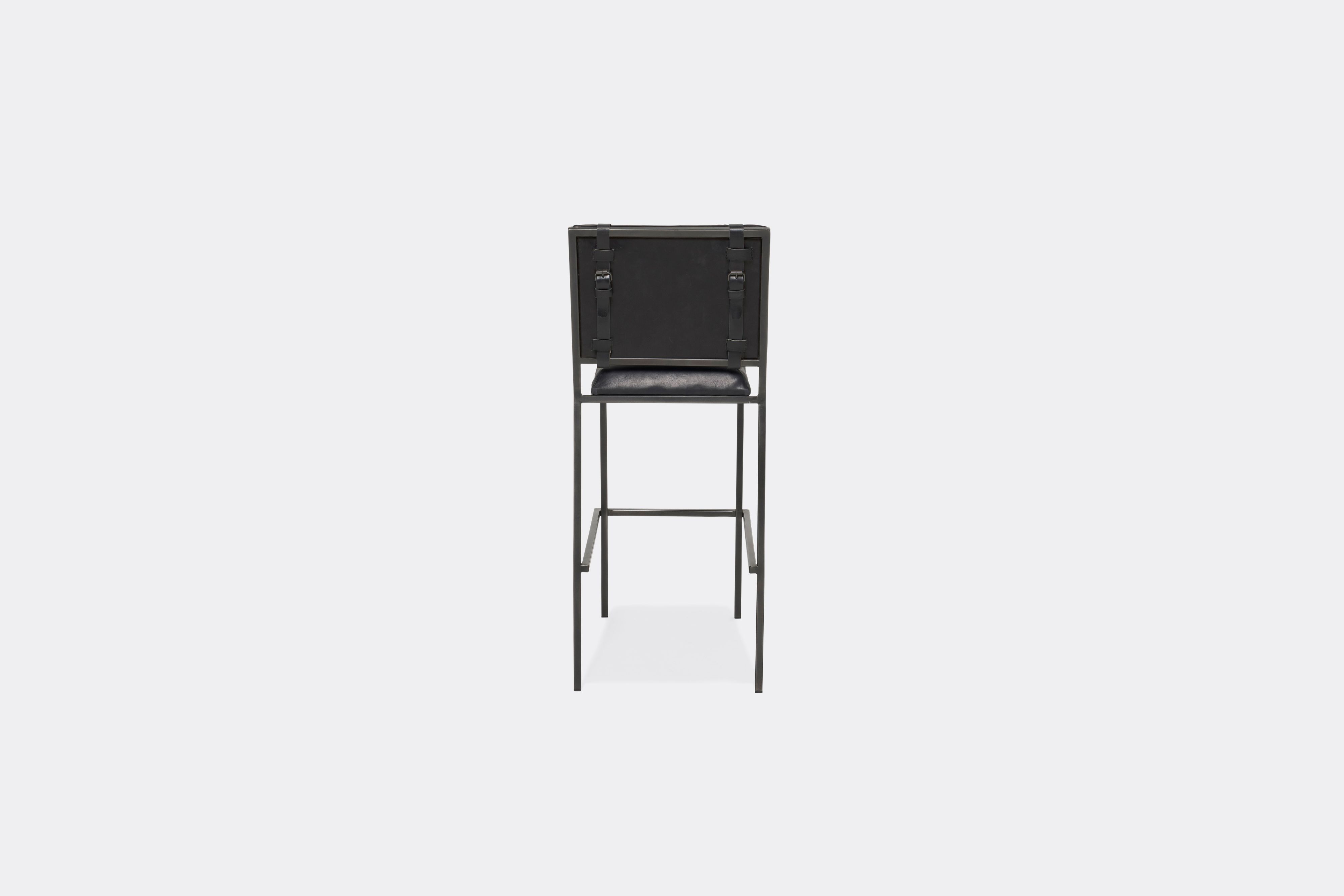 Back of barstool with black leather upholstery and black leather belts on blackened steel metal legs