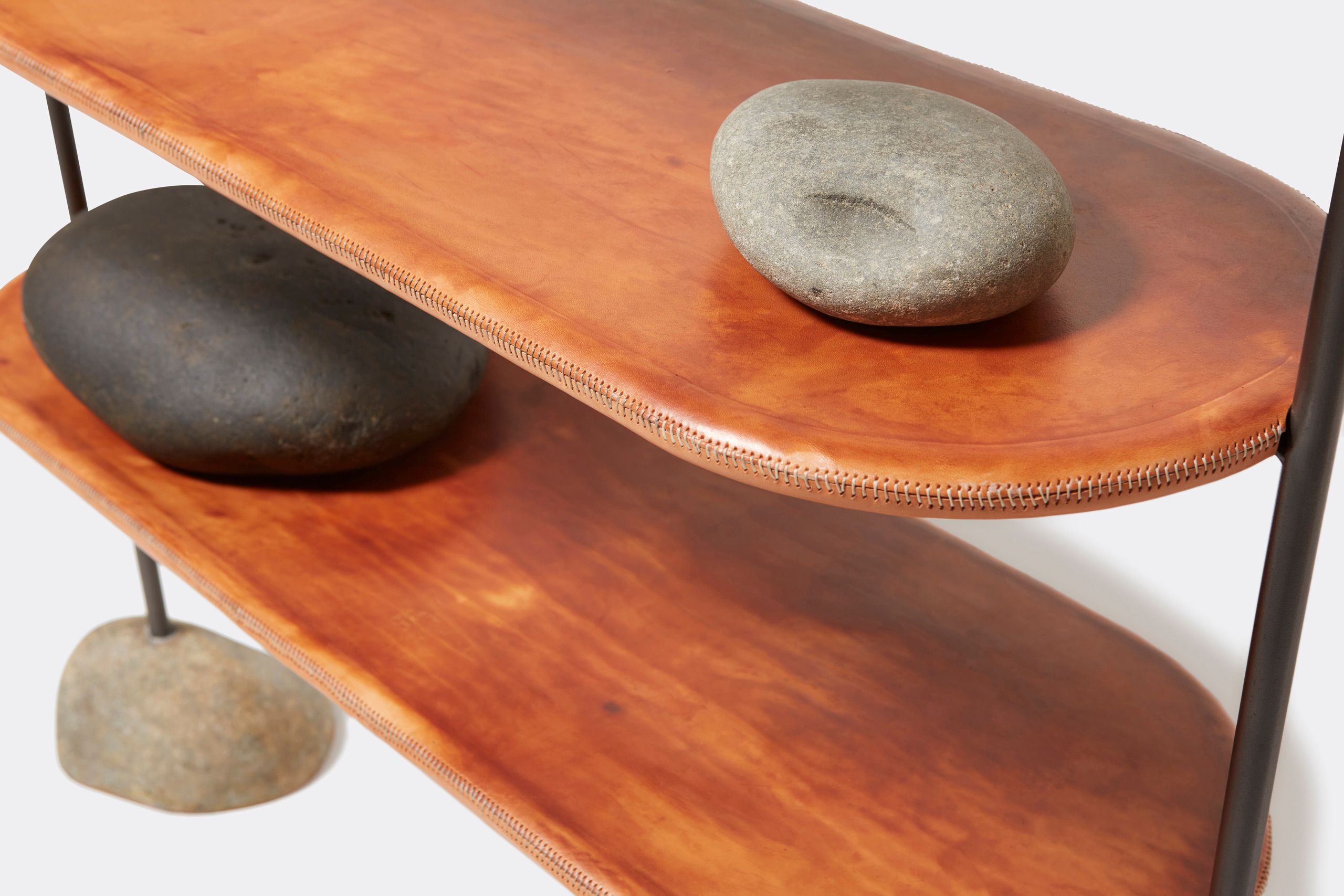 A leather wrapped steel framed shelf with stone bases. Shown on a white background with accent stones