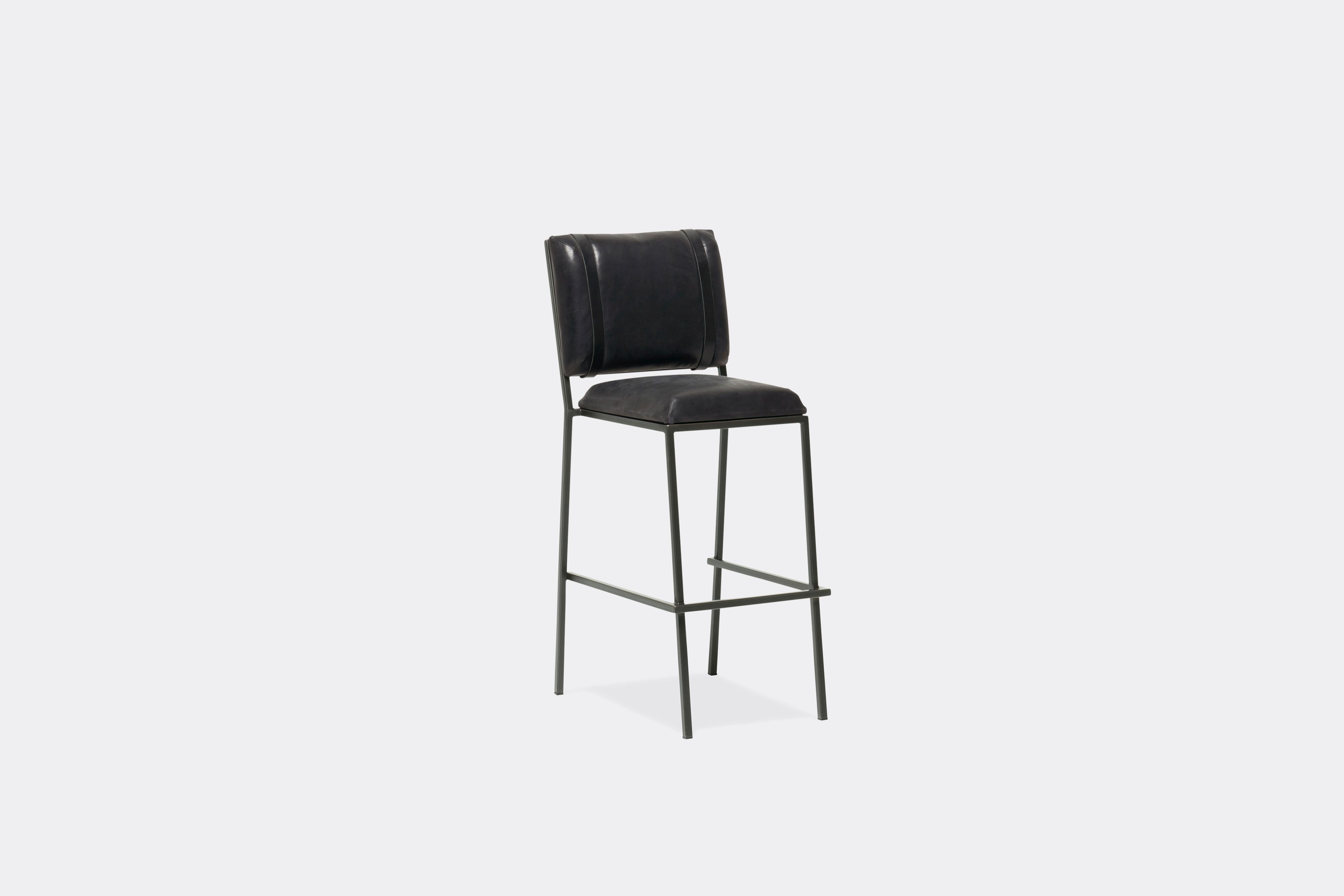 Sideview of barstool with black leather upholstery and black leather belts on blackened steel metal legs