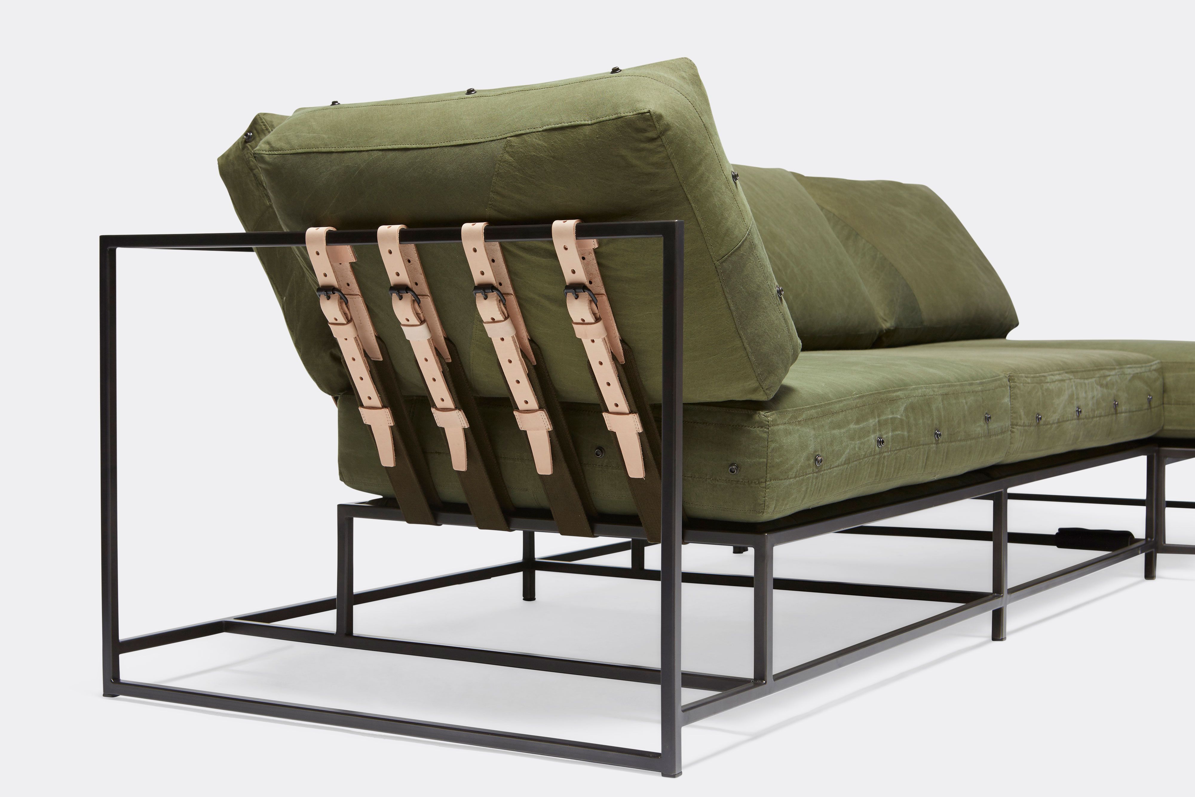 side of sectional with green canvas upholstery and natural tan leather belts on black metal frame