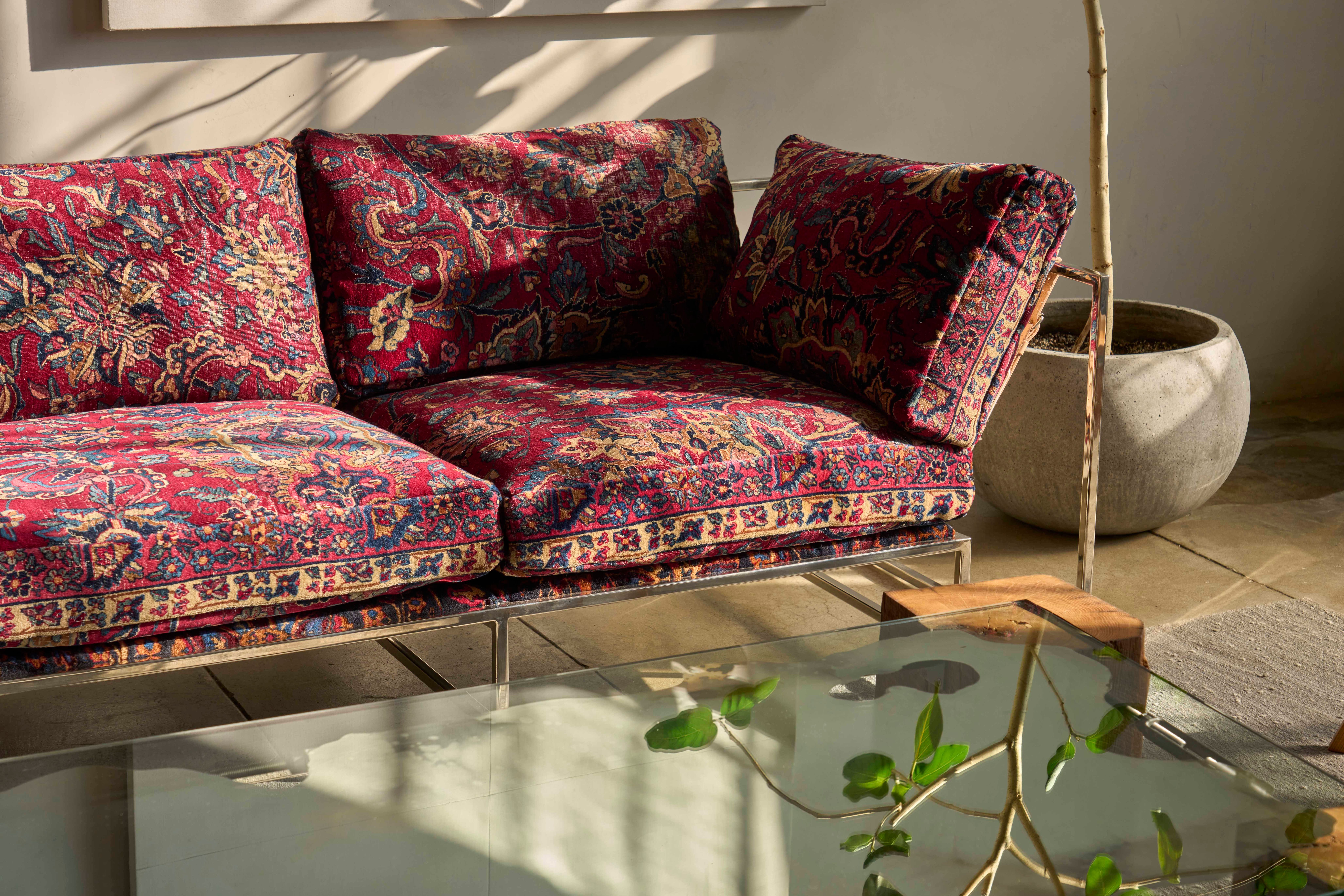 a sofa upholstered in vintage persian rugs is sitting behind a glass coffee table in a living room with natural light
