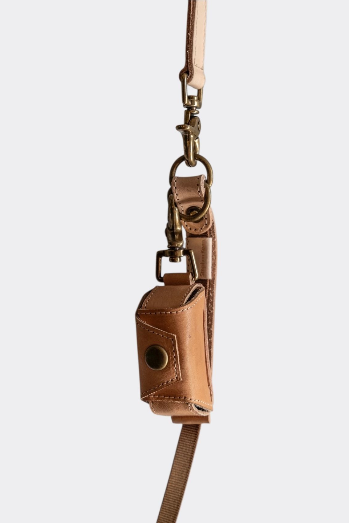 Tan leather poop bag holder case with brass snap, hanging from a tan leather leash.