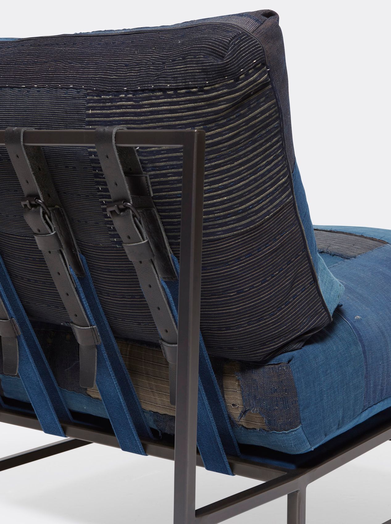 A steel framed chair upholstered with vintage japanese indigo and grey quilted material and blue and black supporting belts shown on a white background