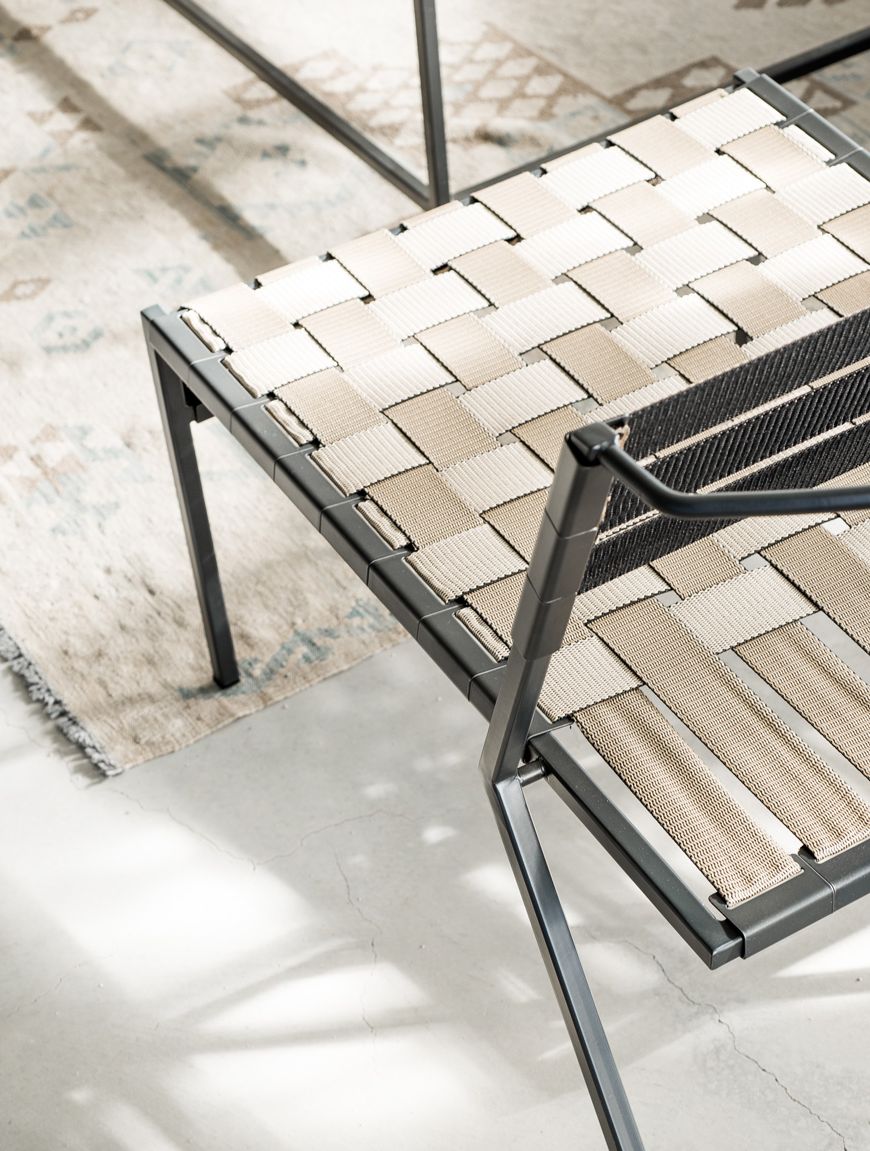 An outdoor steel chair with black metal finish and interwoven tan webbing on a light background