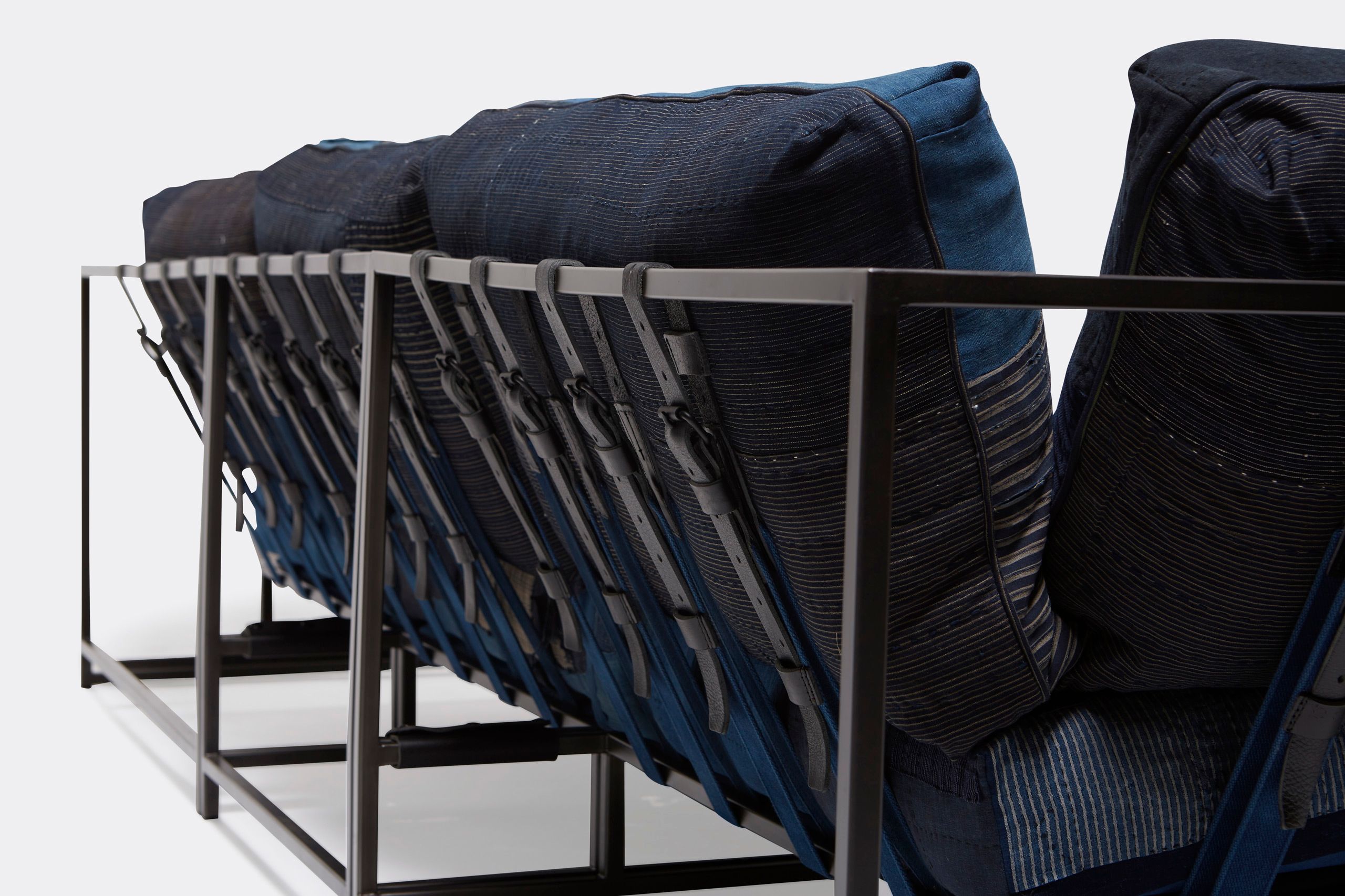 A steel framed sofa with vintage Japanese indigo and grey upholstery and supporting belts shown on a white background