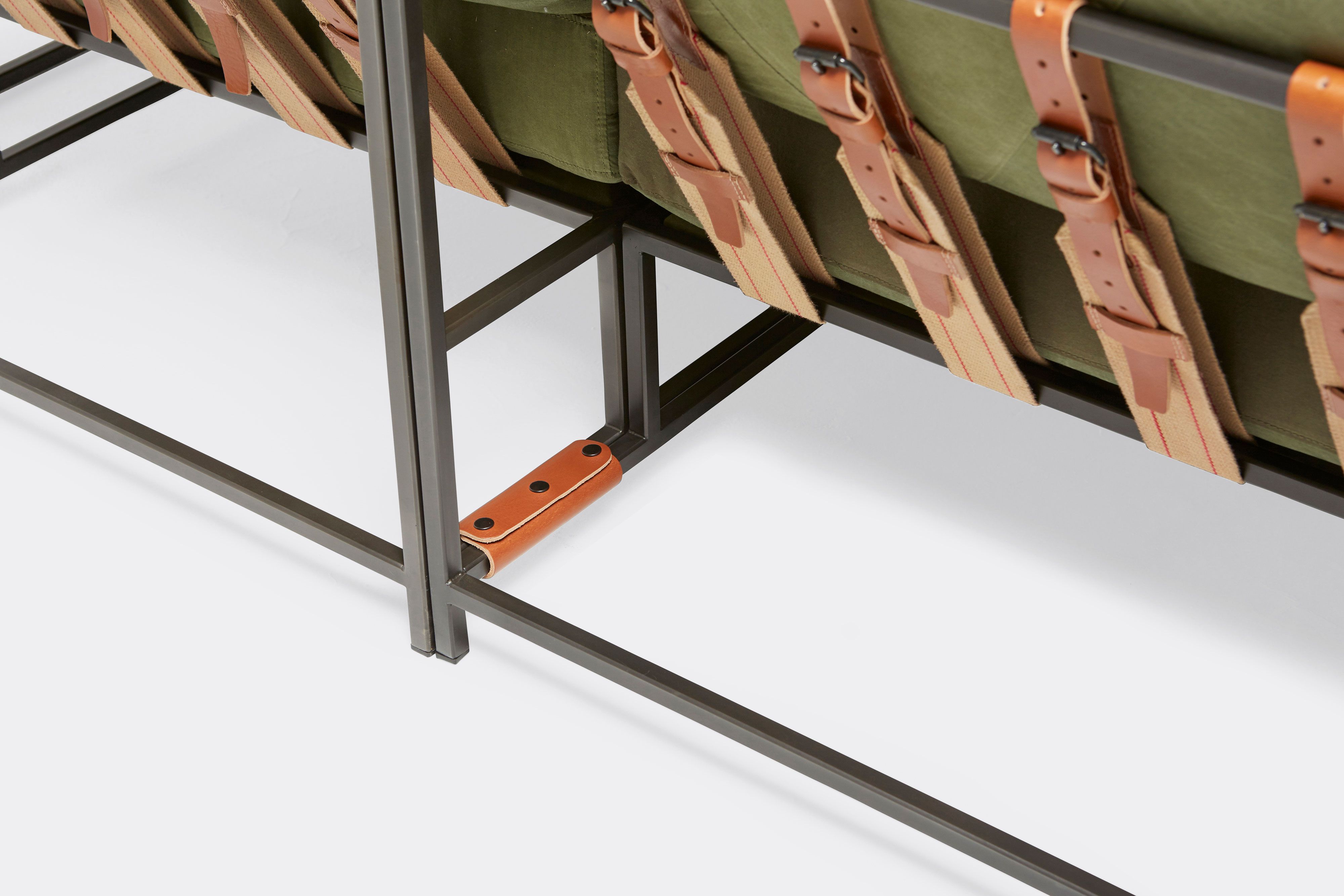 detail of sectional with green canvas upholstery and brown leather belts on black metal frame