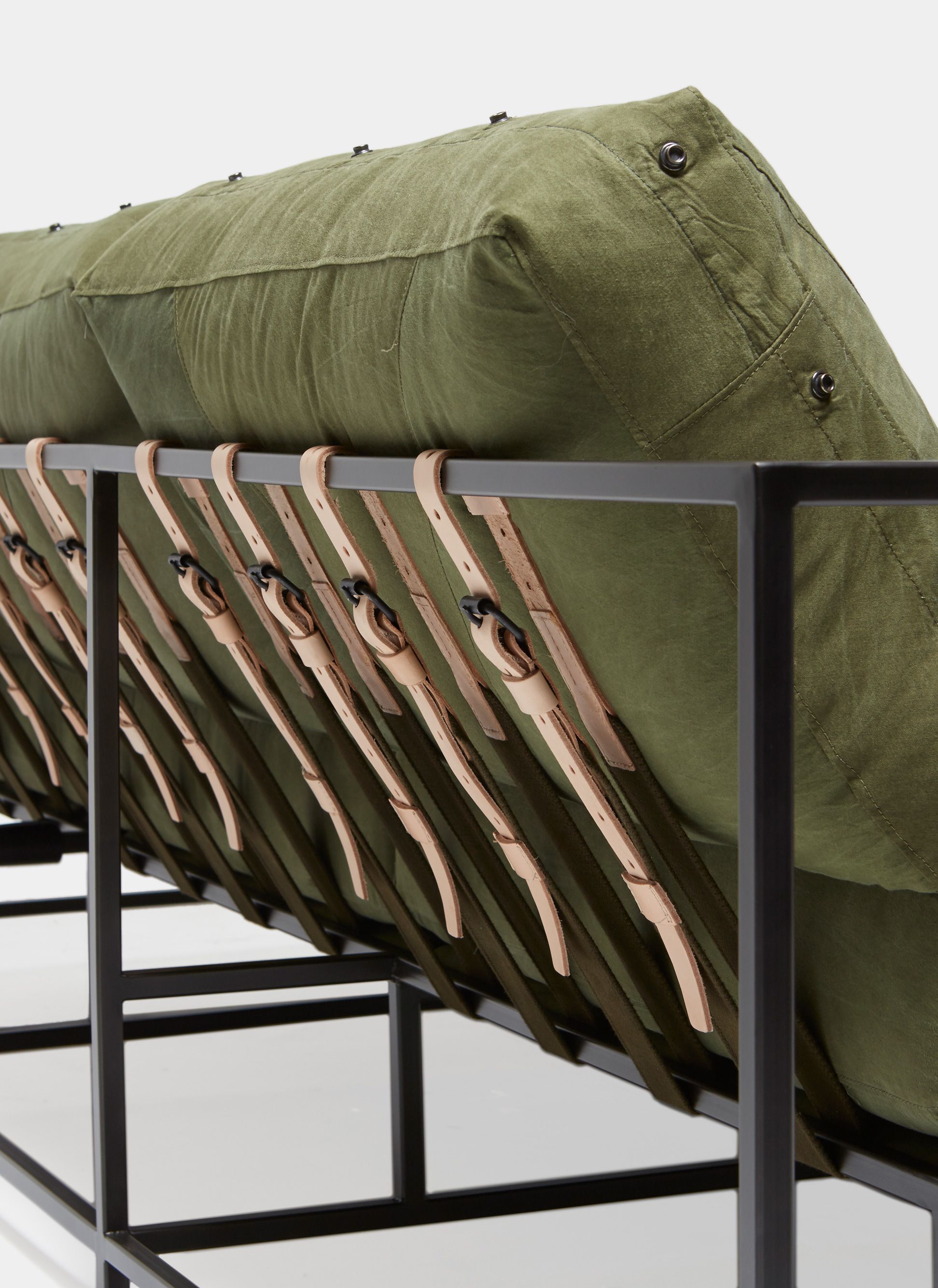 a green canvas sectional sofa with a black steel frame and supporting belts shown on a white background .
