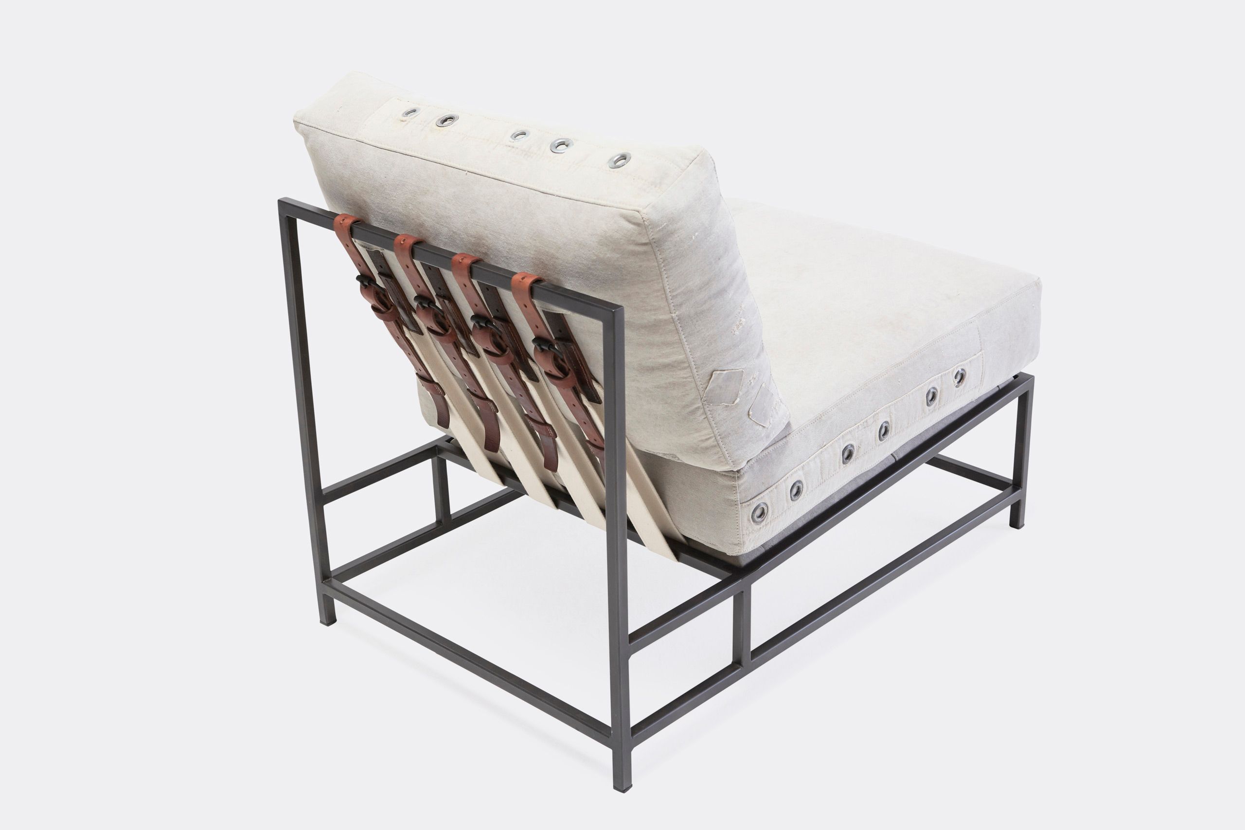 A chair with a white cushion and leather straps atop a blackened steel frame on a white background
