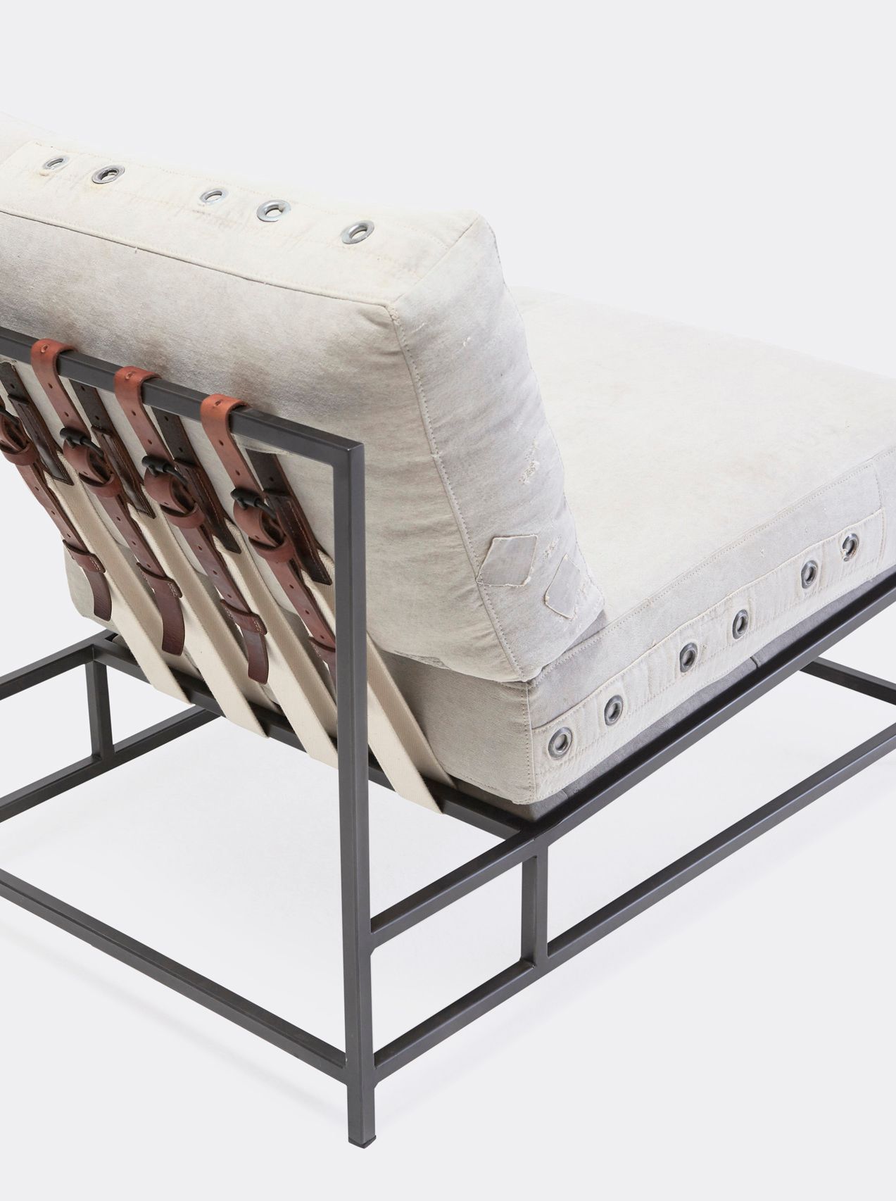 A chair with a white cushion and leather straps atop a blackened steel frame on a white background 
