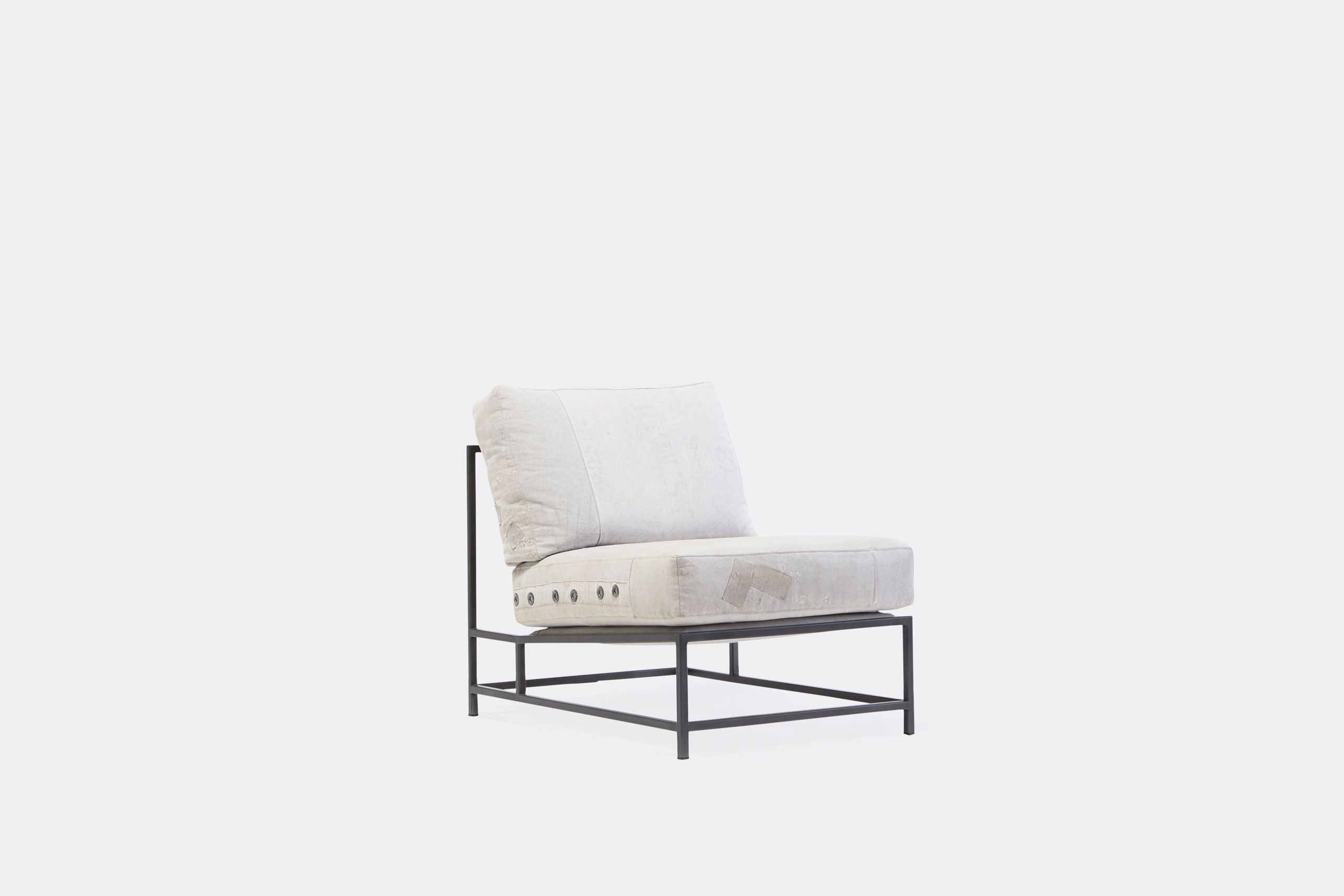 A chair with a white cushion and leather straps atop a blackened steel frame on a white background