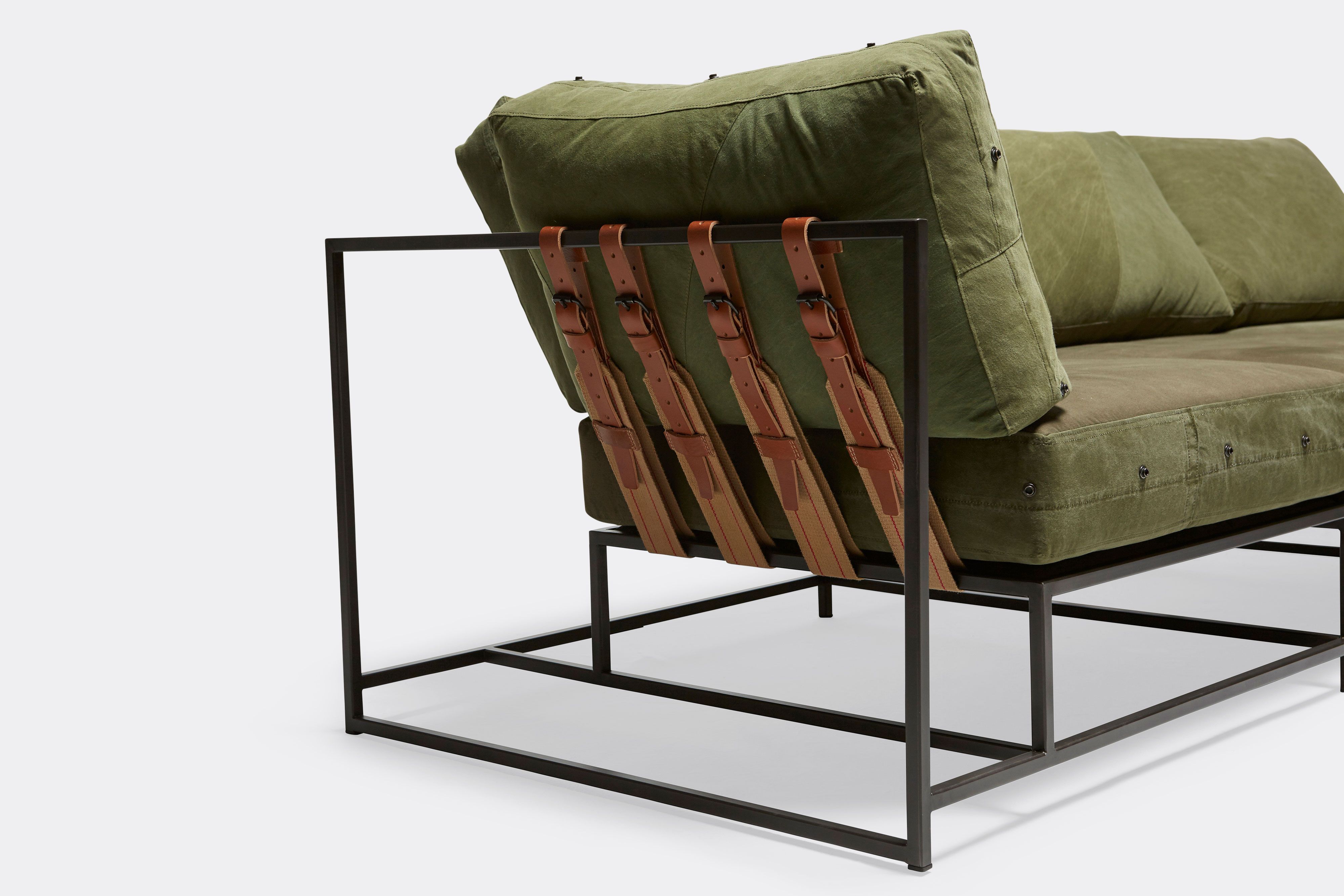 side of sectional with green canvas upholstery and brown leather belts on black metal frame