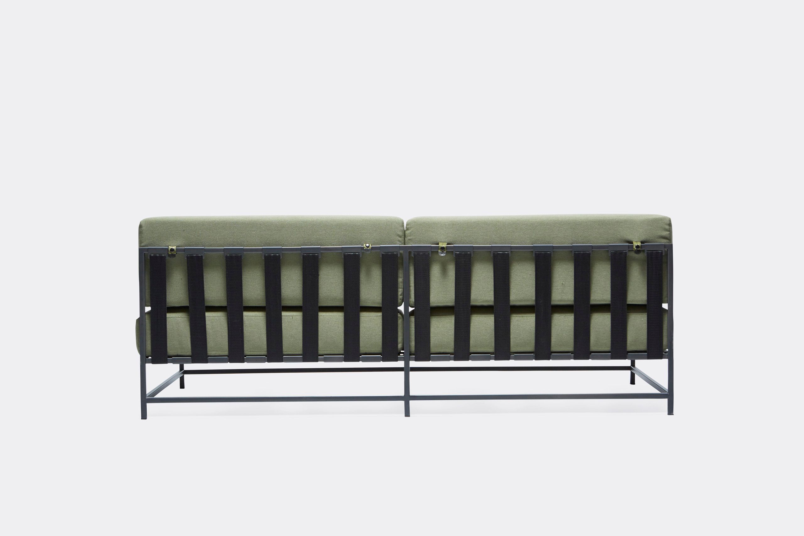a steel framed sofa with black metal finish and green cushions and supporting belts on a white background .